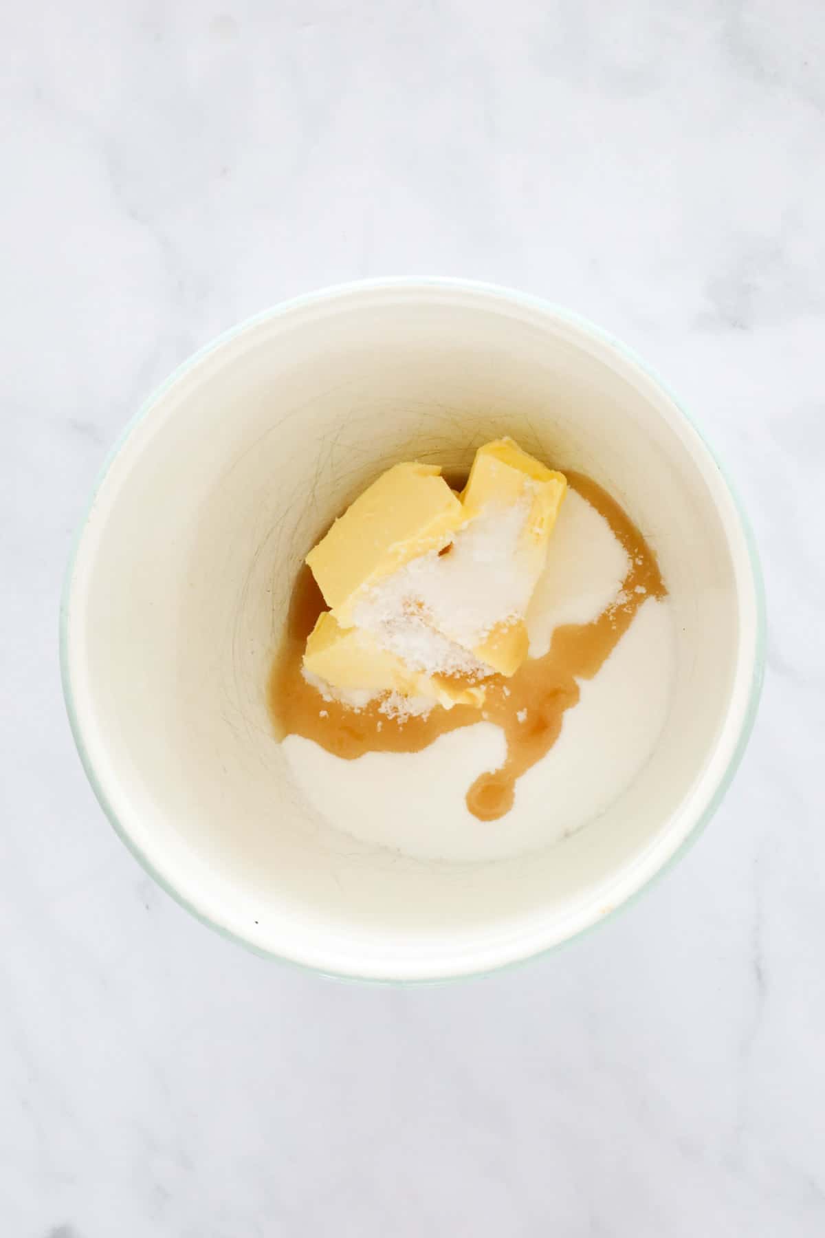 Butter, sugar and vanilla extract in a white mixing bowl.