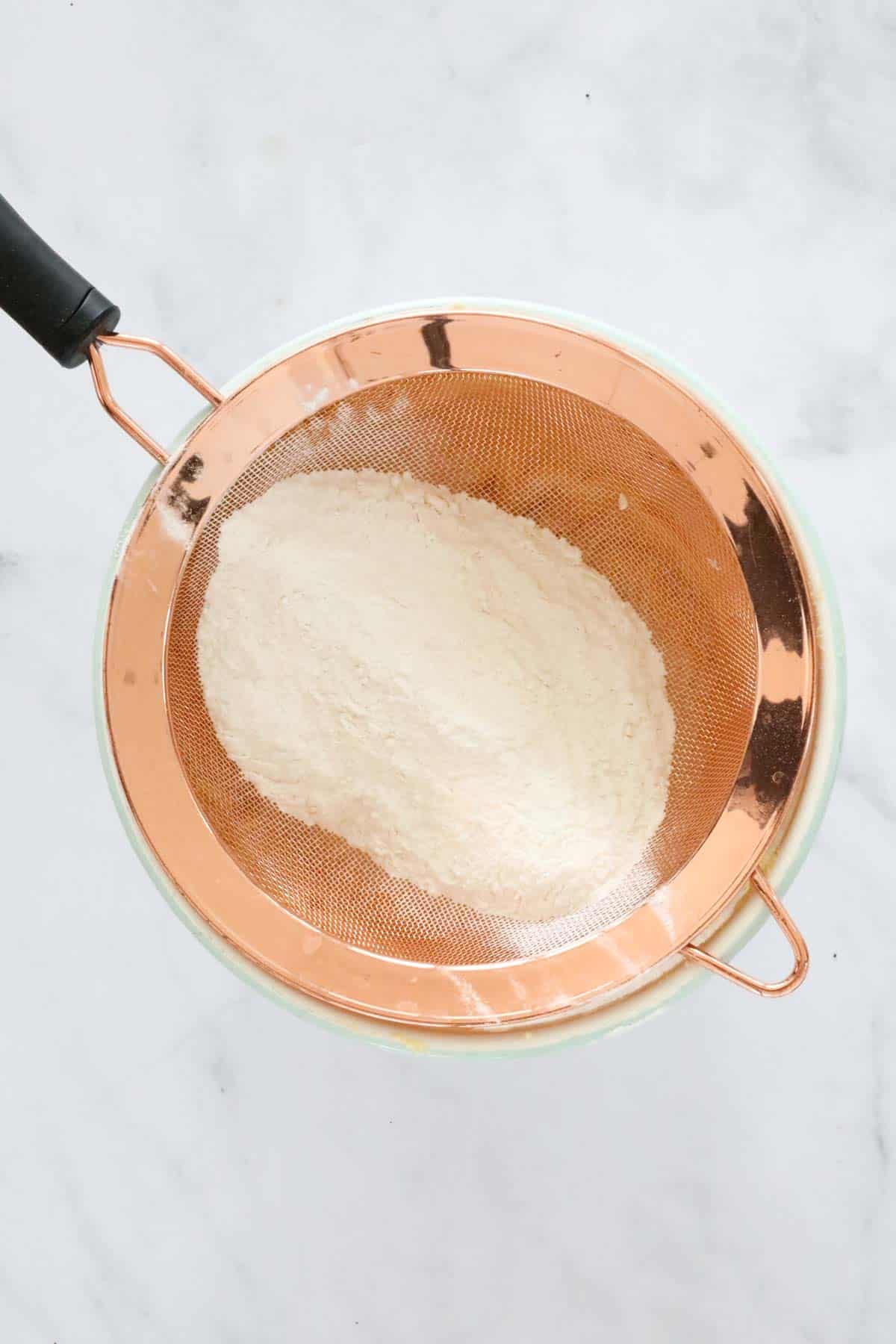 Flour in a copper sieve placed over a bowl.