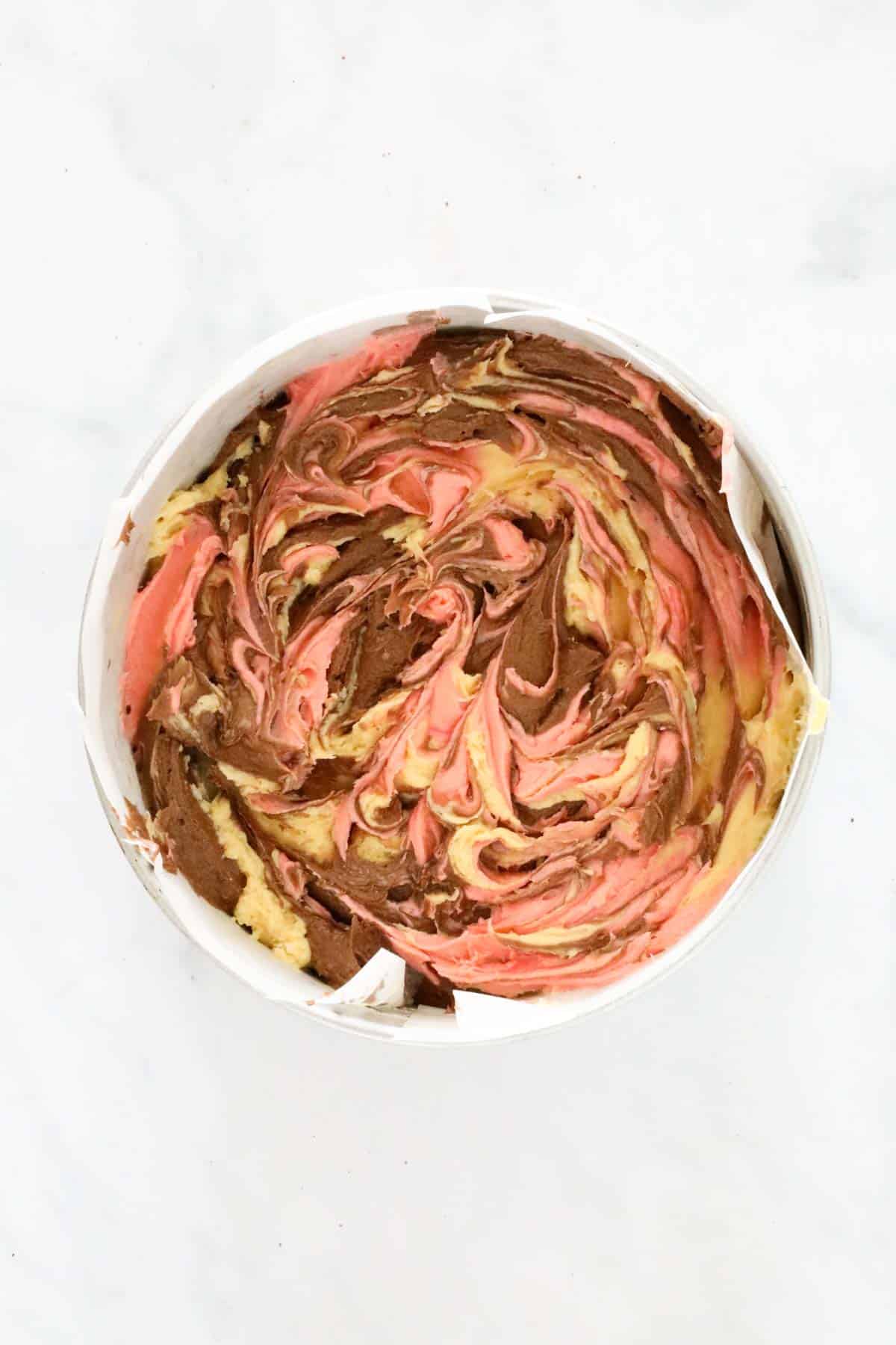 The three colours of cake batter swirled to create a marble pattern.