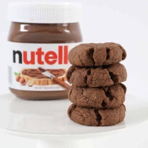 A stack of Nutella cookies in front of a jar of Nutella.