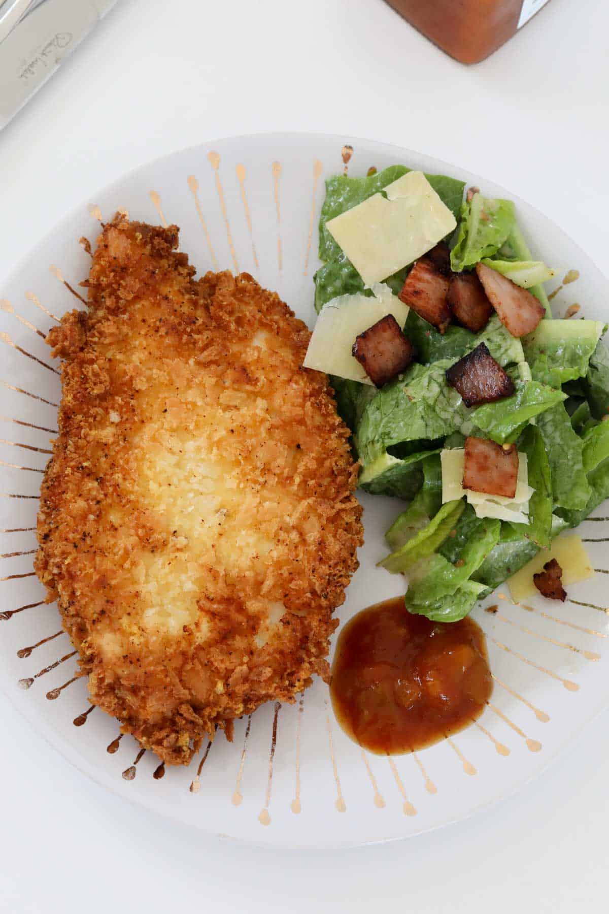 A crispy schnitzel on a plate with a caesar salad.
