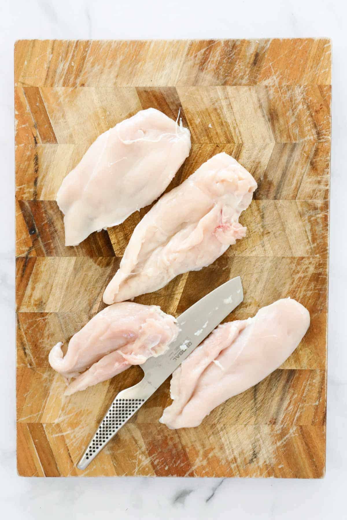 Raw pieces of chicken breast on a cutting board.