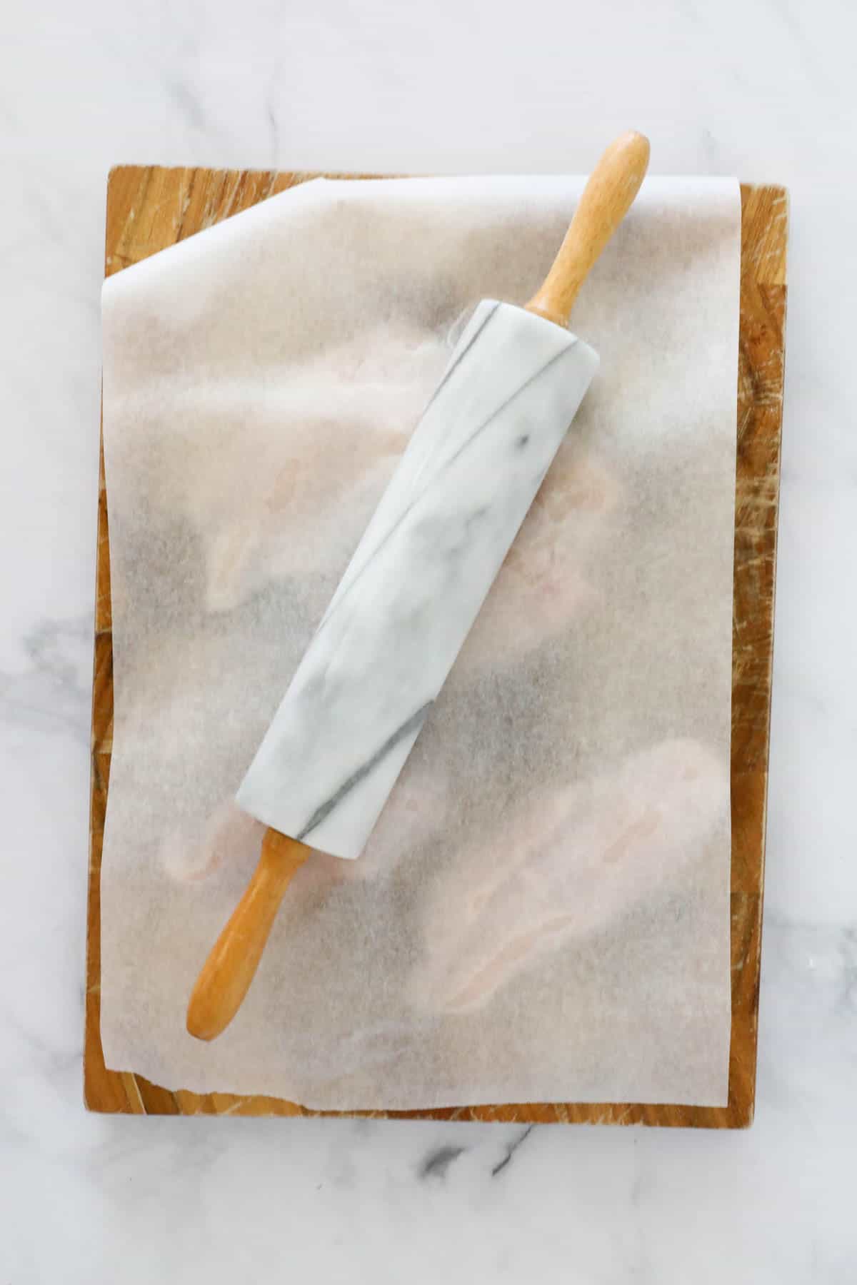 A rolling pin placed on top of baking paper covering fillets on a cutting board.
