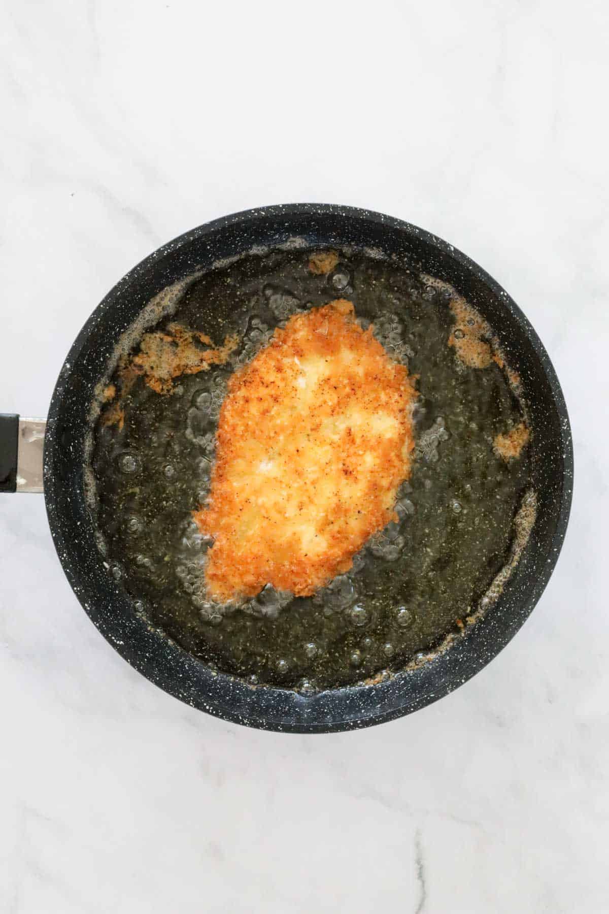 Breaded chicken being fried in oil in a pan.