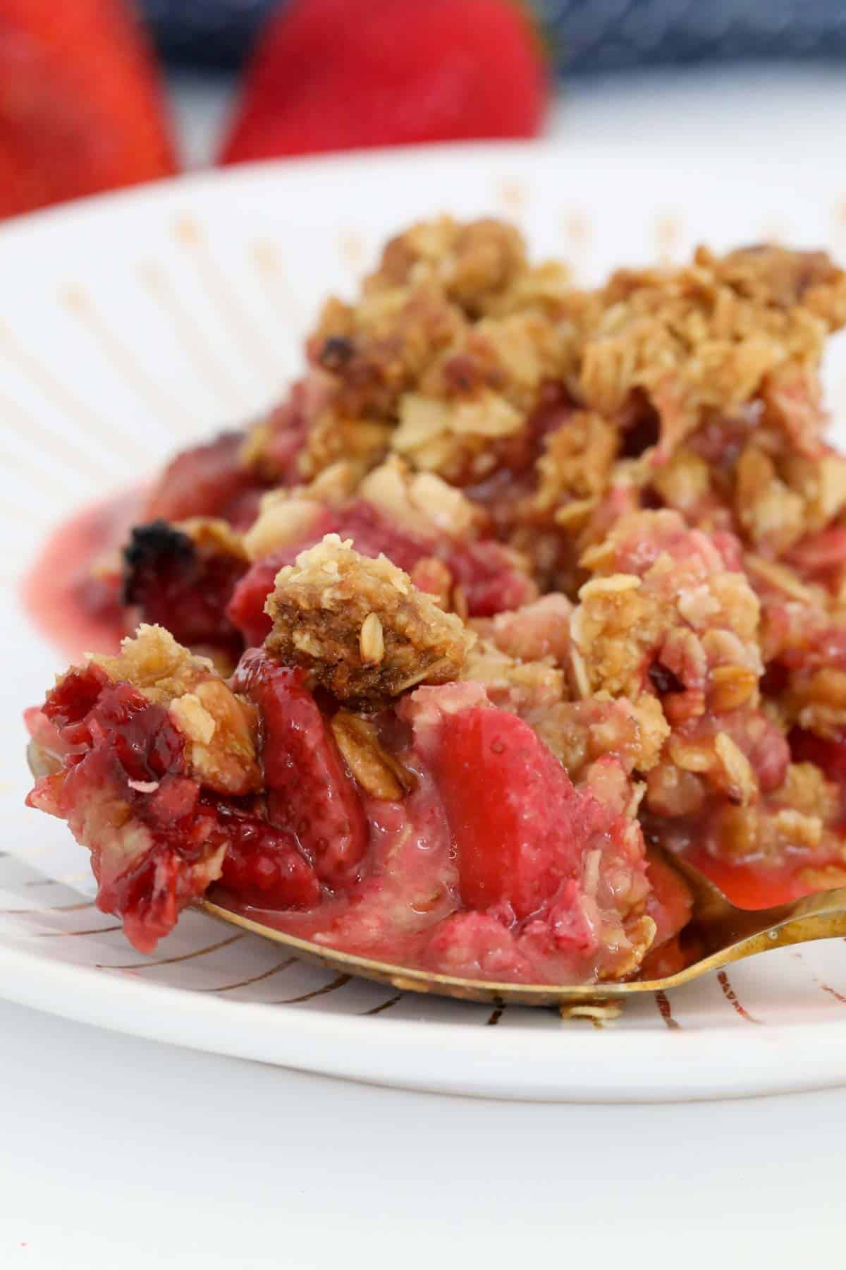 A close up of a spoonful of baked fruit dessert with crunchy rolled oat topping on a plate.