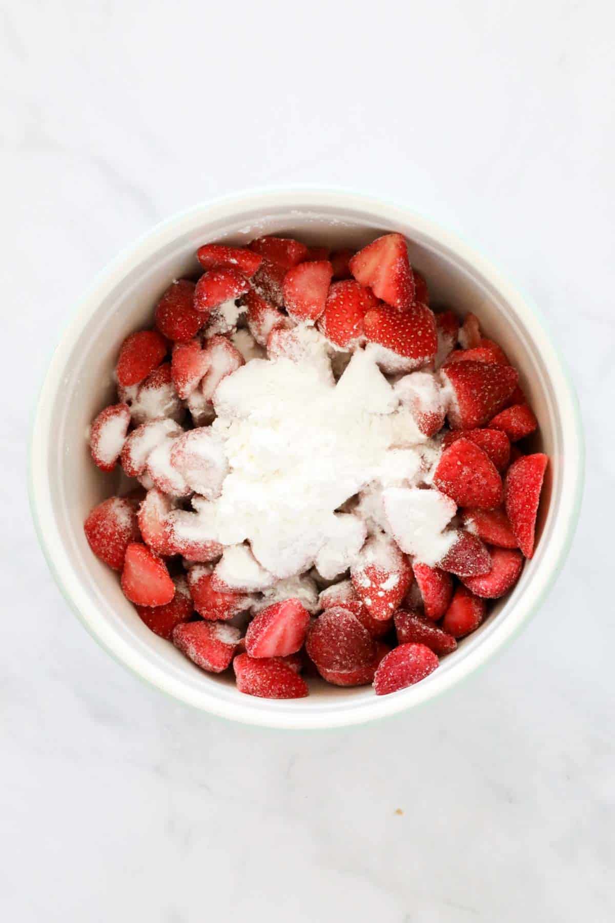 Strawberries, cornflour and sugar in a white bowl.