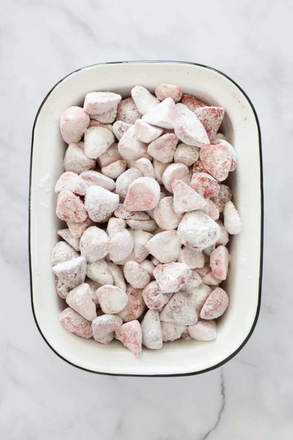 Strawberries coated with sugar and cornflour in a white baking dish.