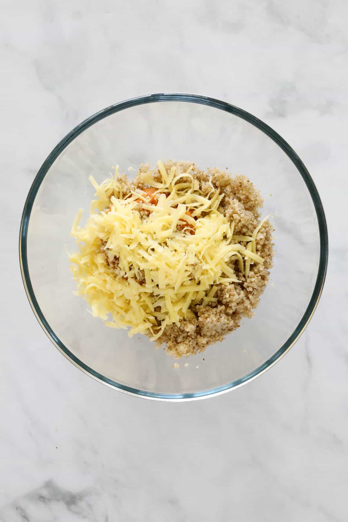 Cold mashed sweet potato, cooked quinoa and grated cheese in a bowl.