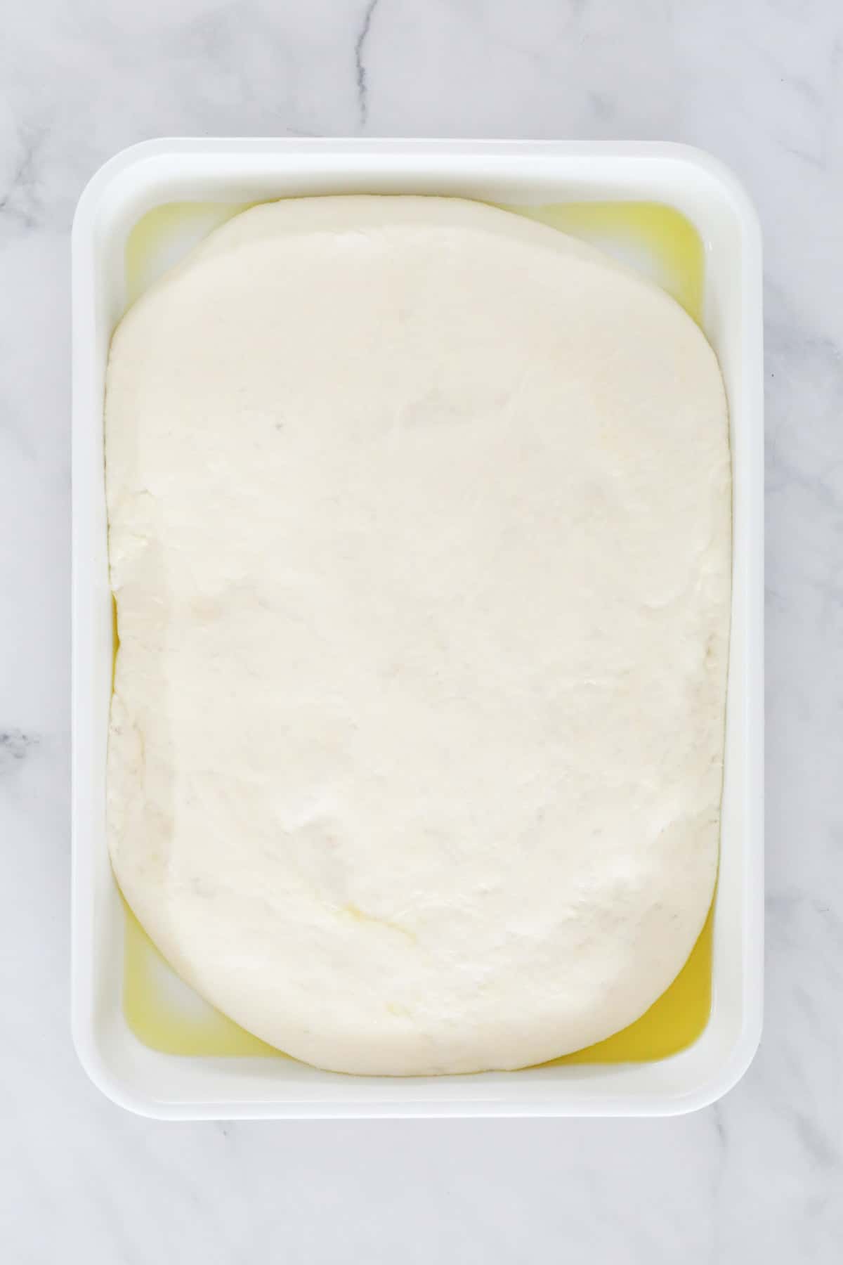 Dough in a white dish with oil in the base.