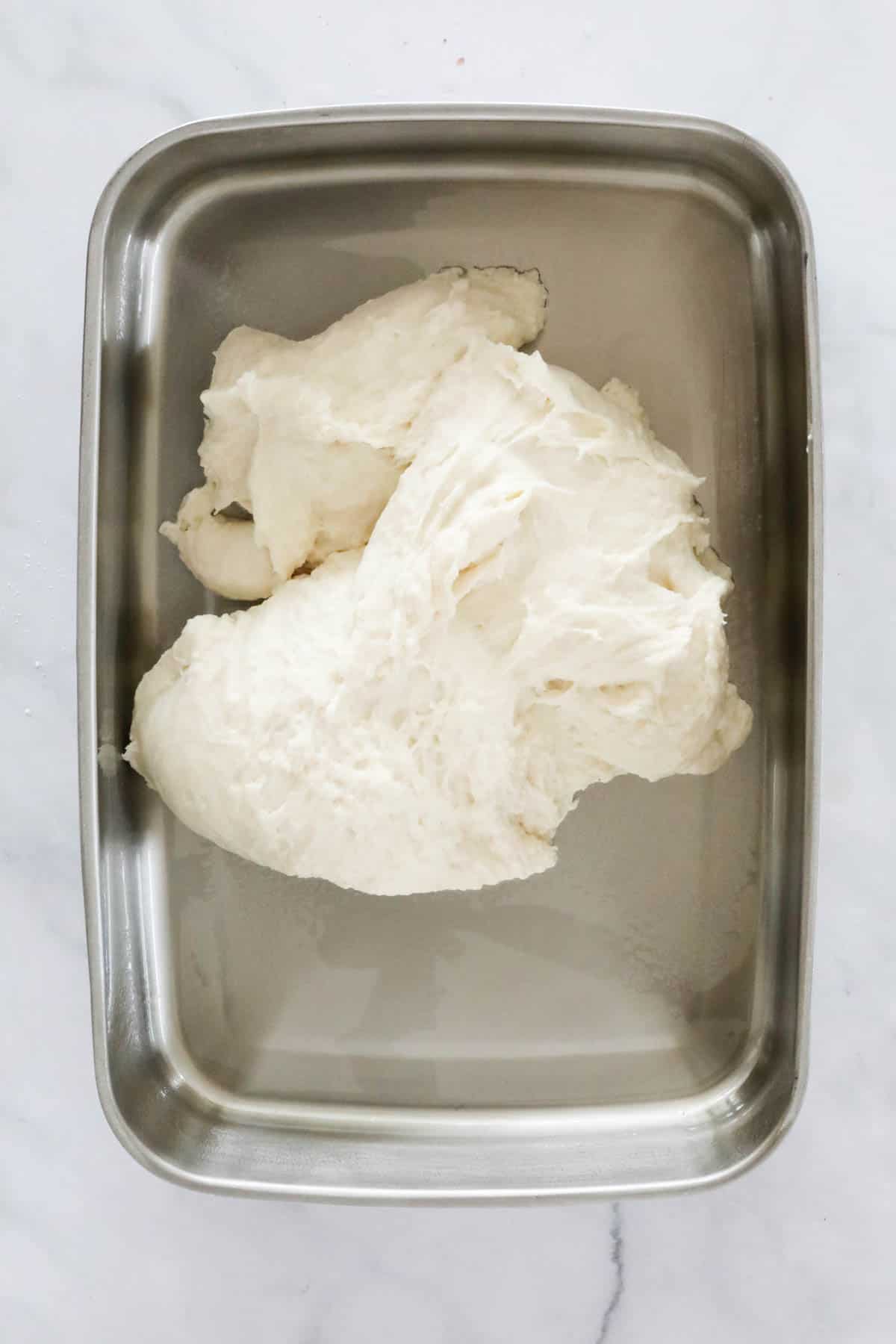 White dough in a rectangular stainless dish.