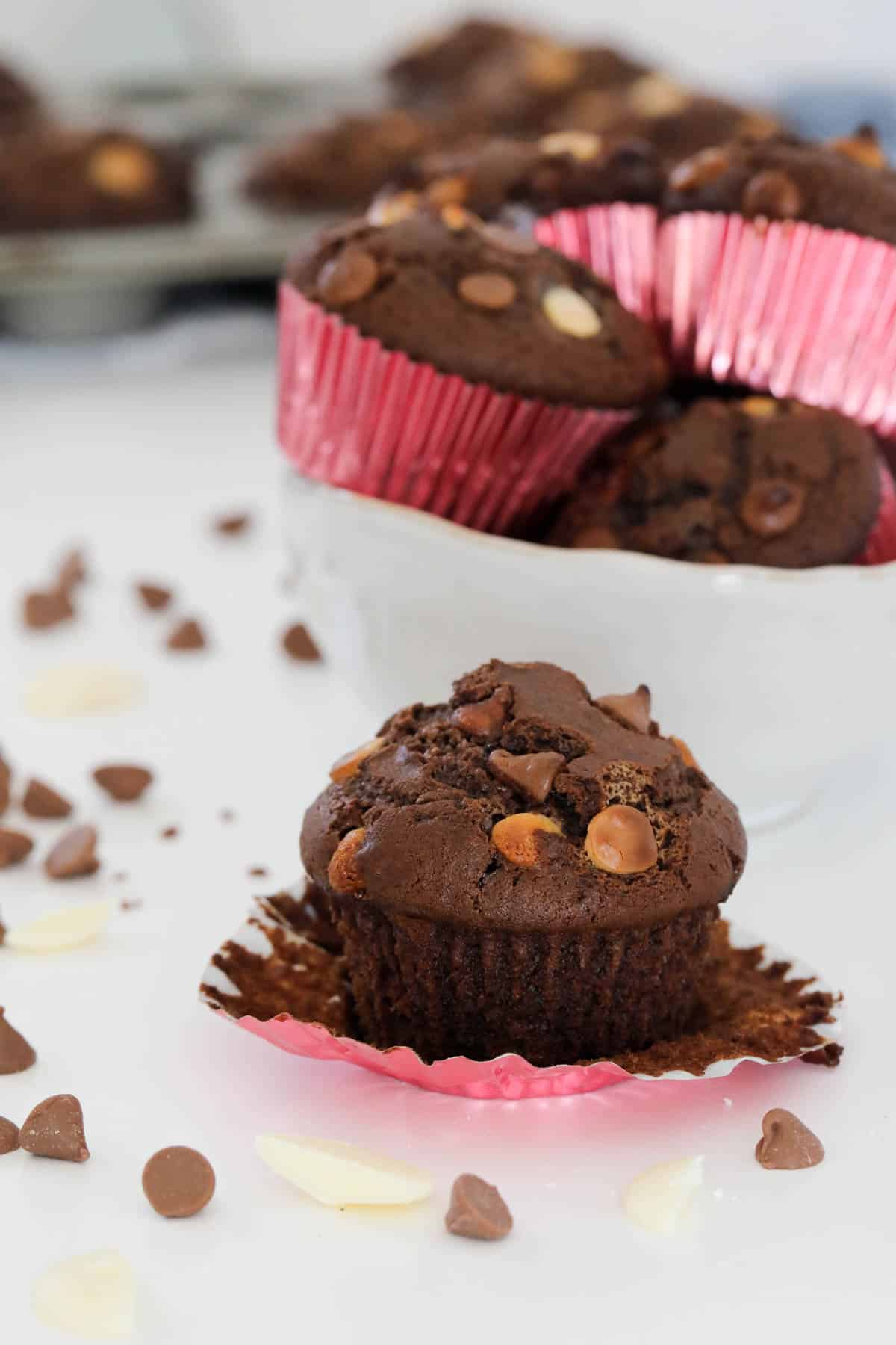 A chocolate muffin with the paper case removed, chocolate chips scattered around the surface.
