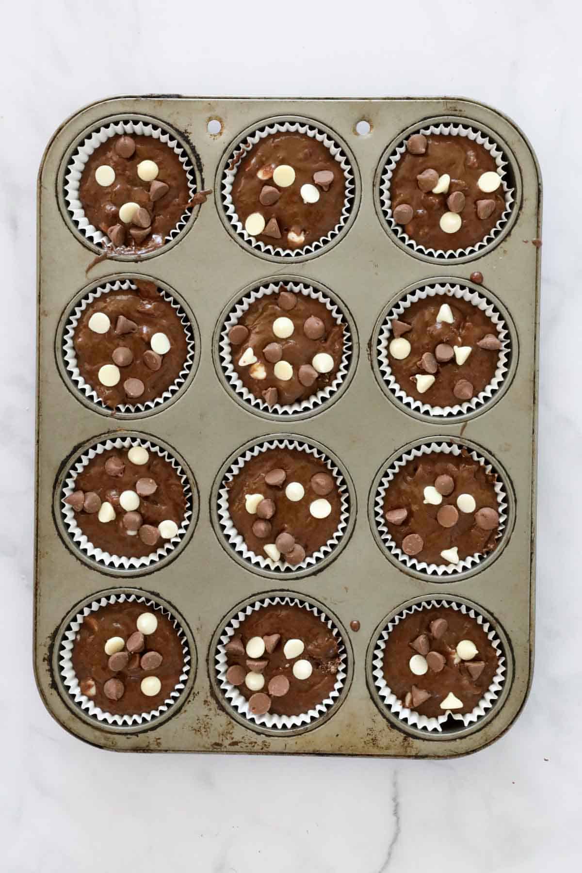 Muffin batter spooned into paper muffin cases. The batter sprinkled with extra milk and white chocolate chips.