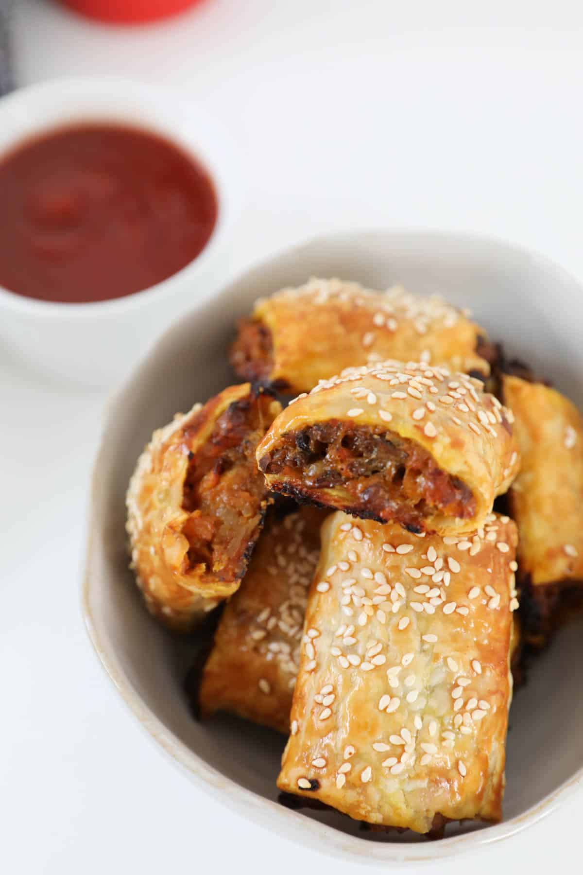 Lentil sausage rolls in a white bowl with a small bowl of sauce in the background.