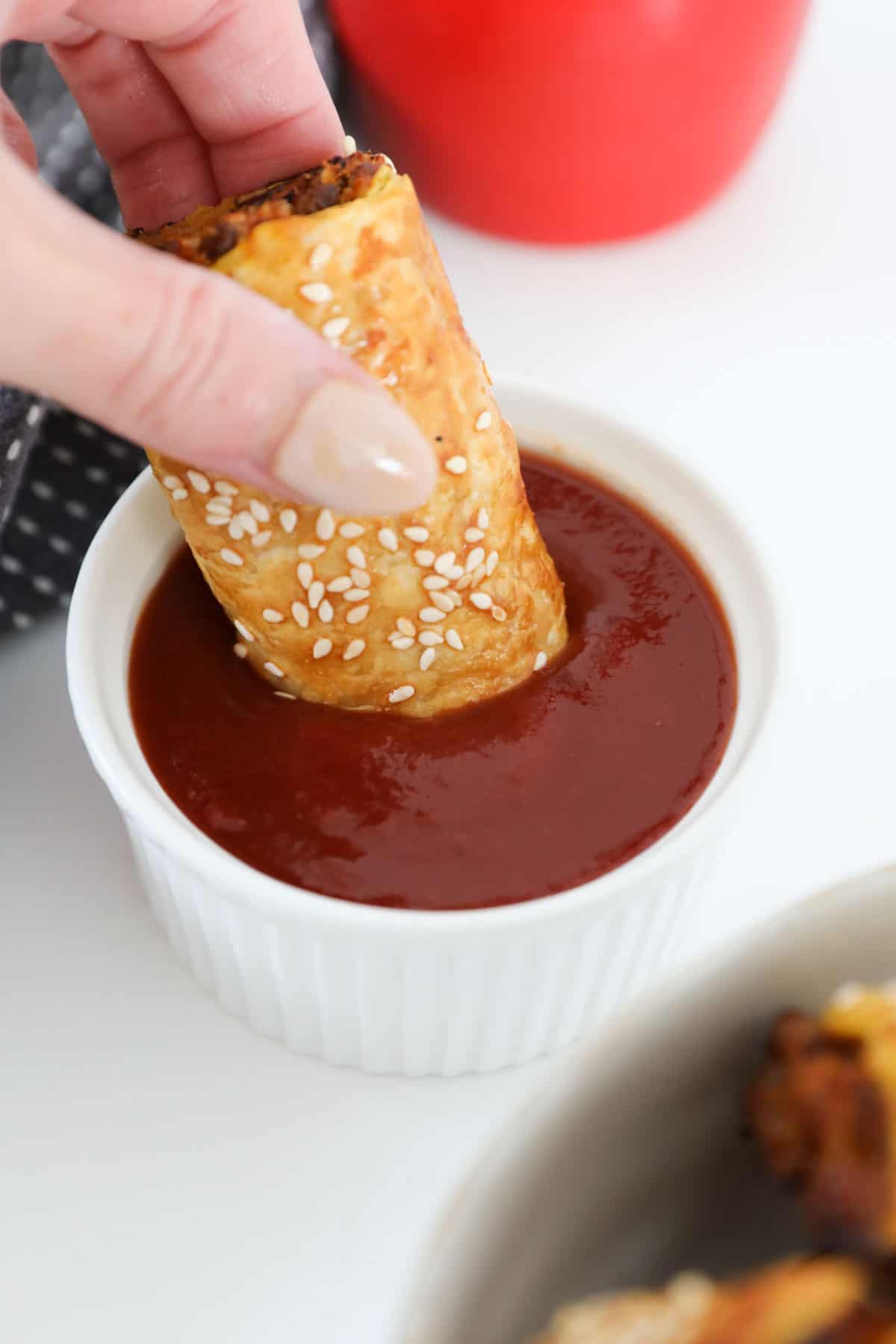 A vegetarian sausage roll being dipped into a small bowl of tomato sauce.
