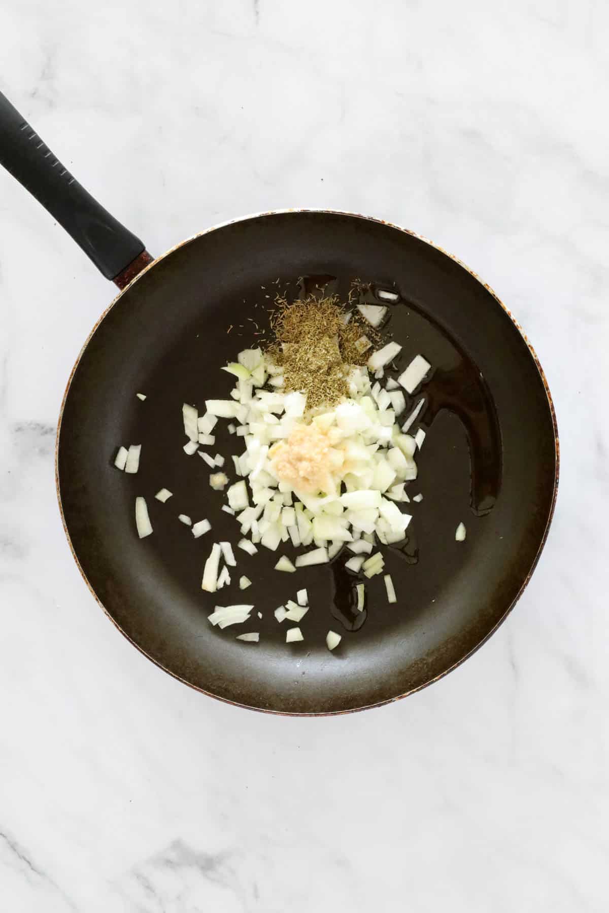 Onion, garlic and dried herbs in a frying pan.