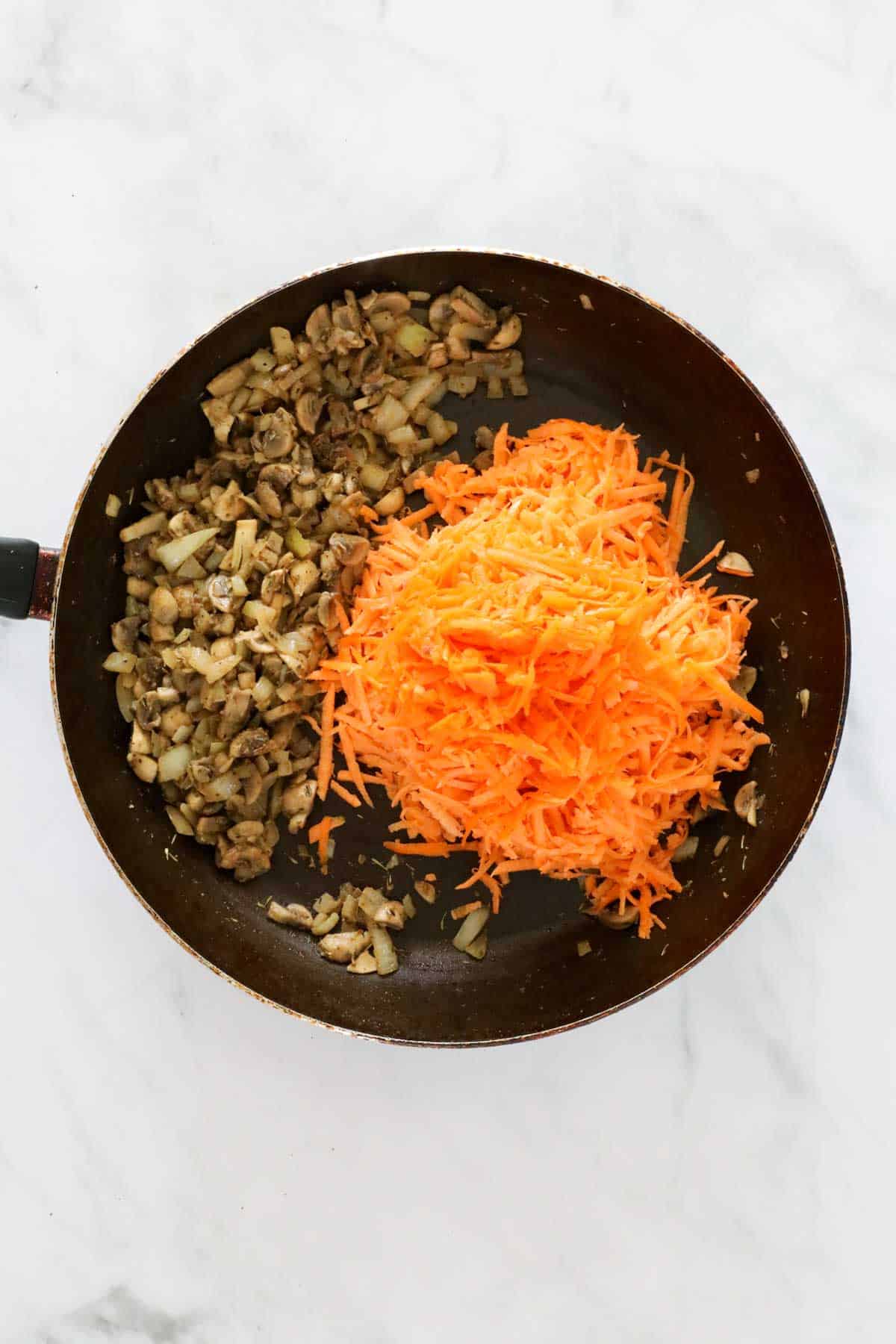 Grated sweet potato and grated carrot added to cooked mushrooms and onion in a frying pan.