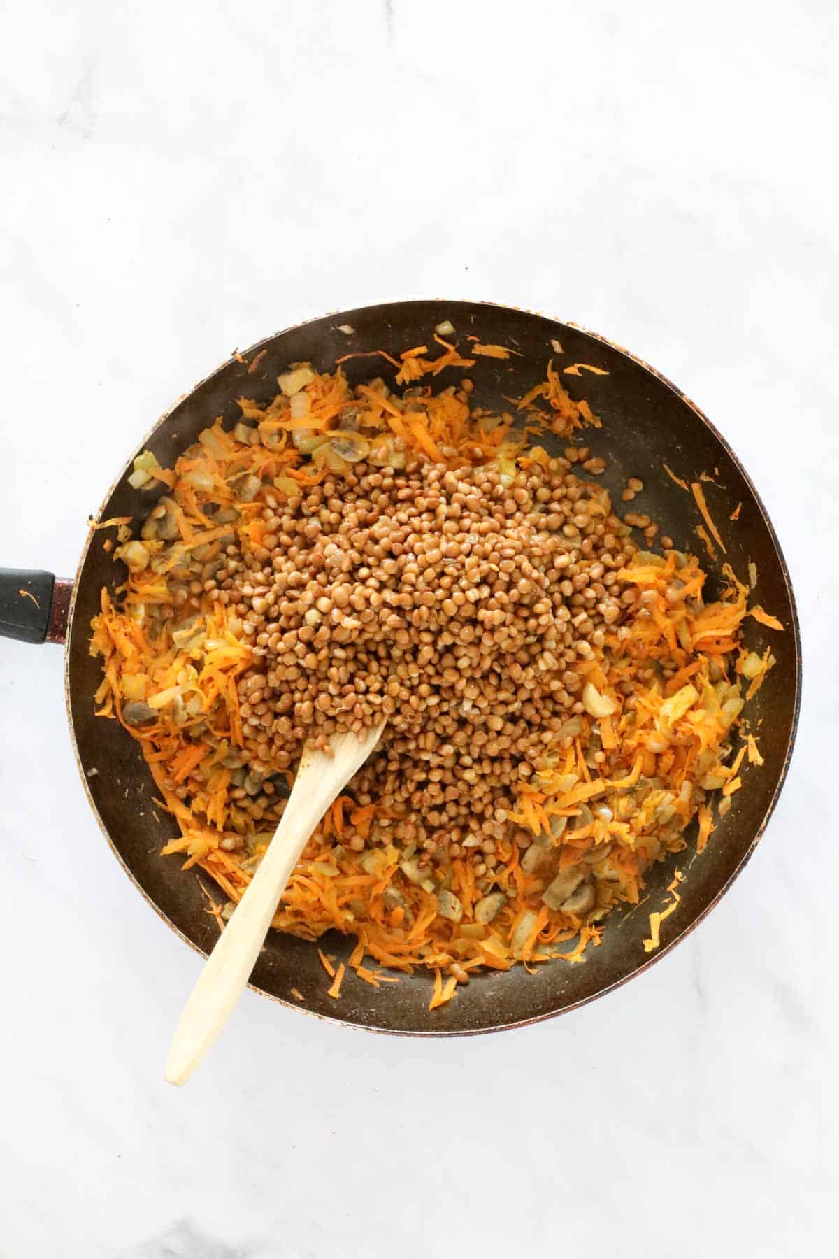 Lentils and soy sauce added to the cooked vegetables in a frying pan.