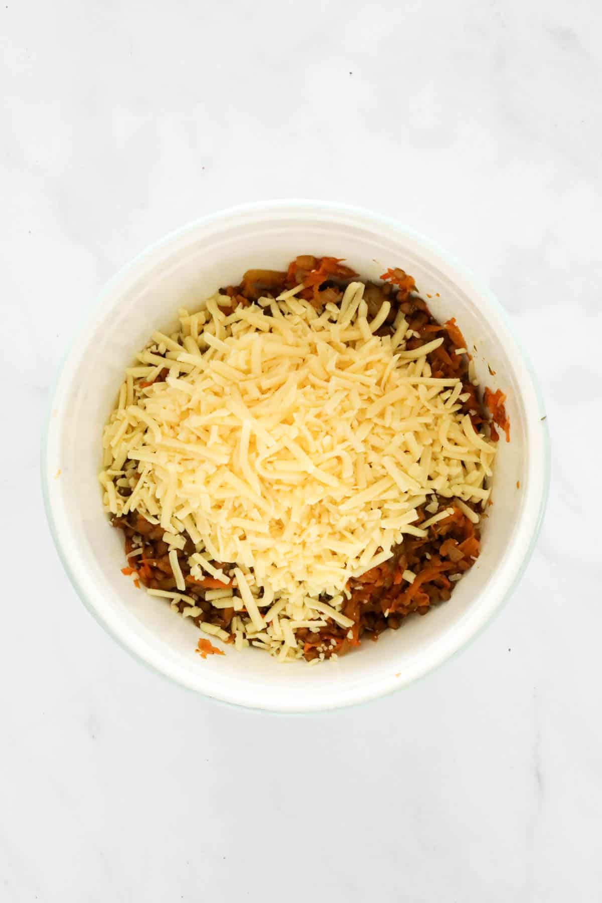 Grated cheese on top of cooled lentil and vegetable filling in a white bowl.