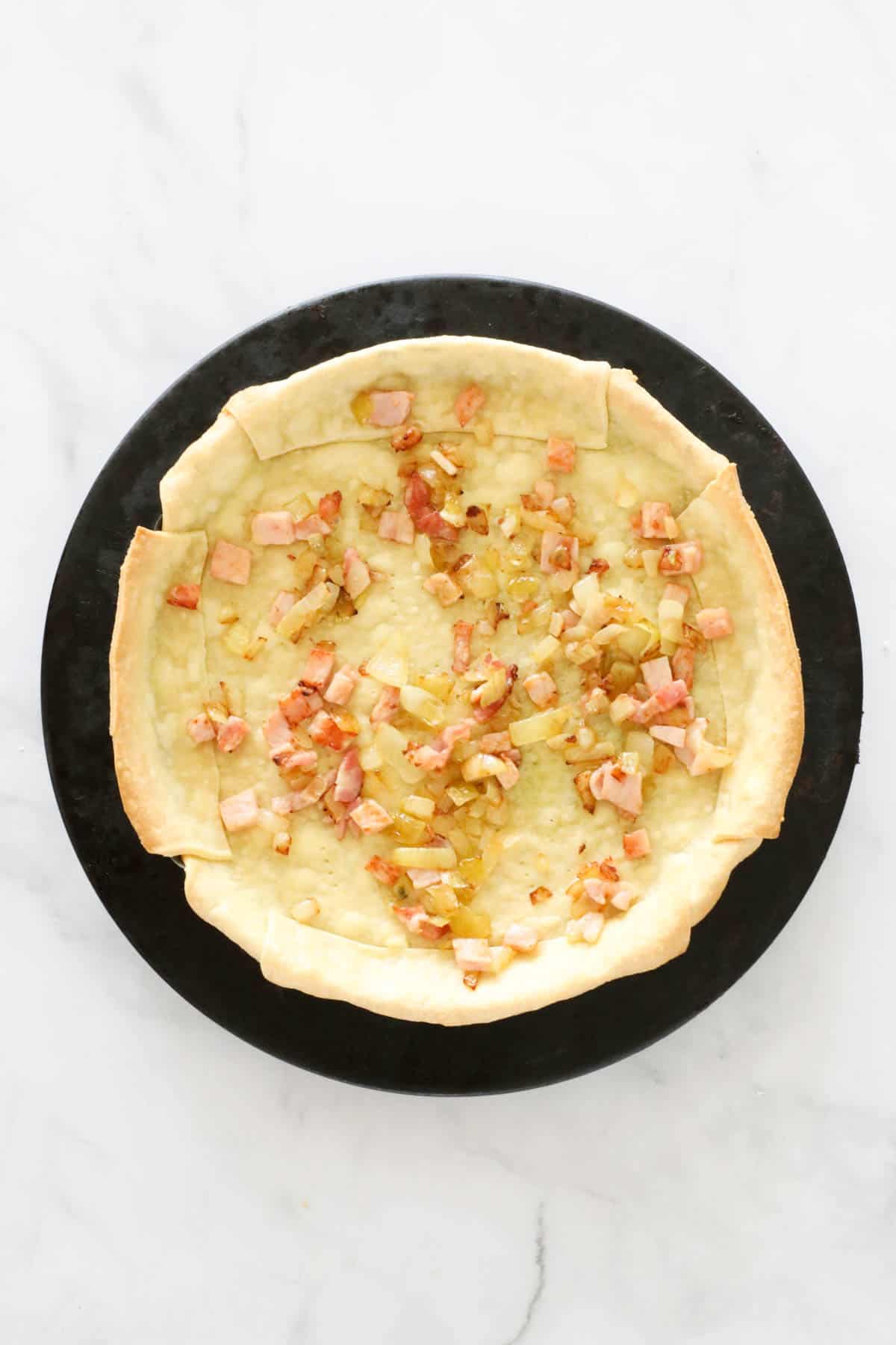 Crust with sauteed bacon and onion sprinkled over the base.
