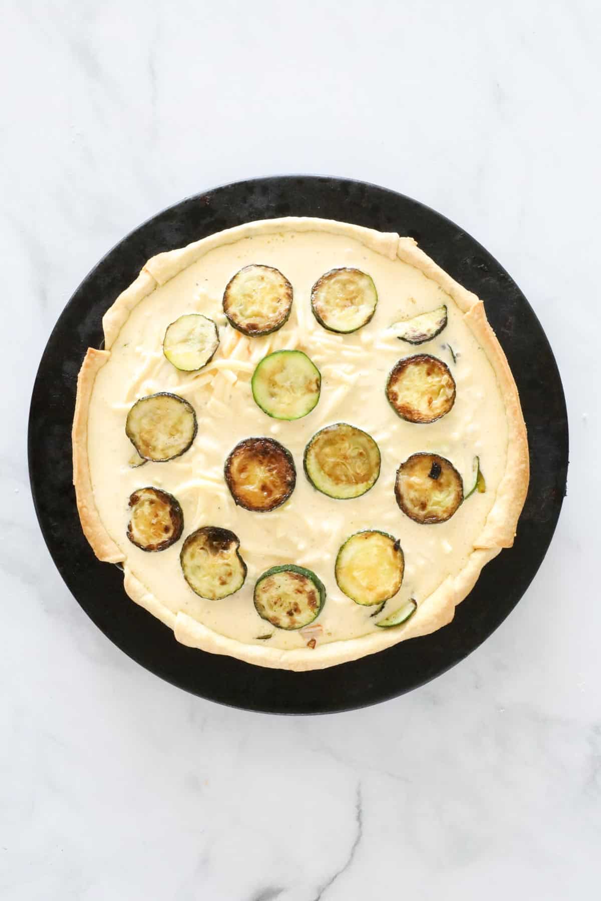 Unbaked quiche in a pan with extra slices of zucchini on top.