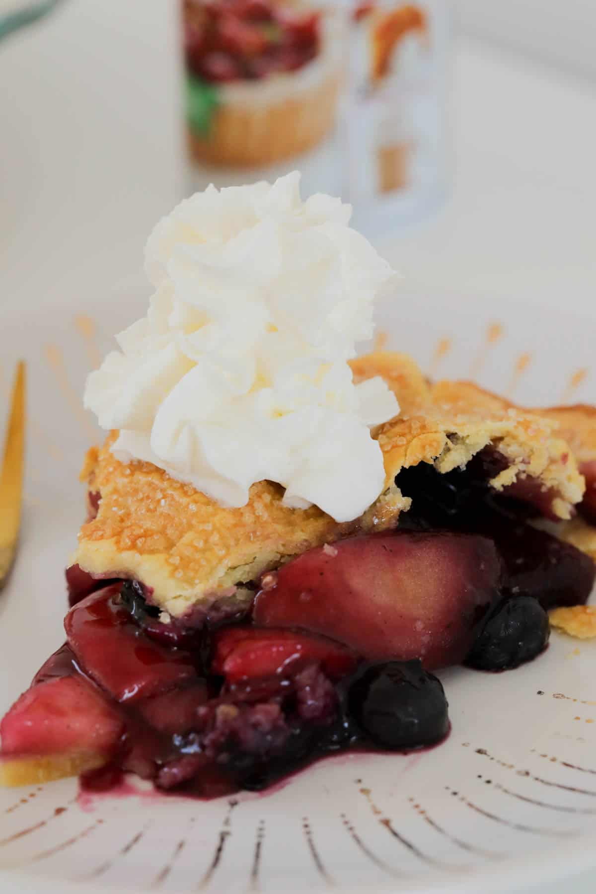 A close up of a slice of blueberry apple pie topped with whipped cream.
