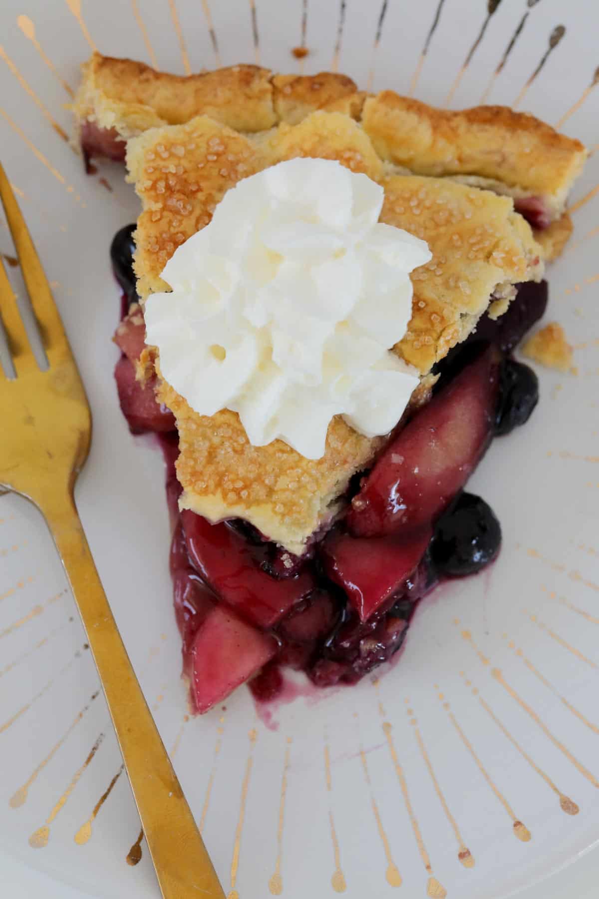 A serve of apple and berry pie with a gold fork beside it.