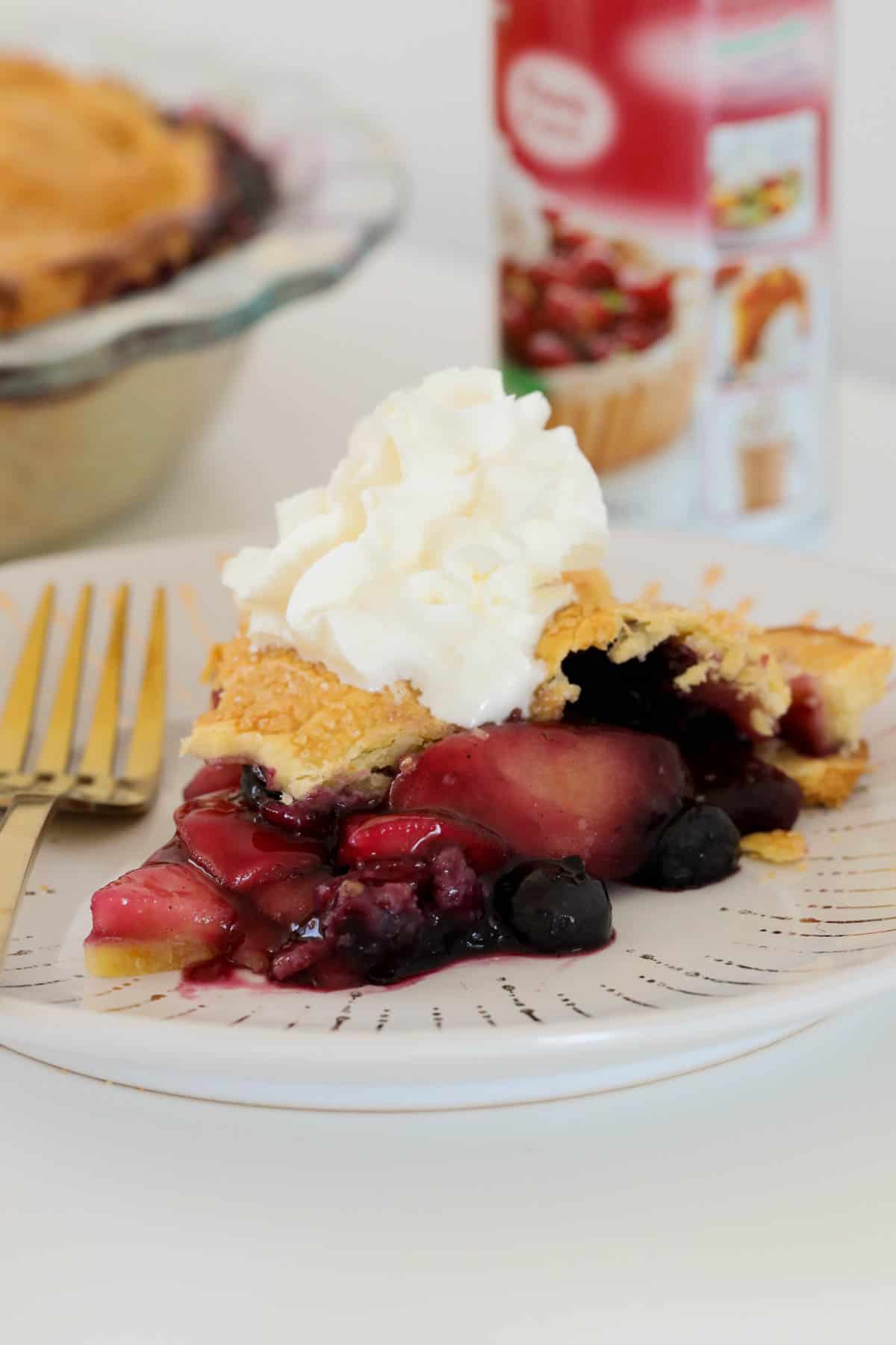 A slice of apple blueberry pie on a plate served with cream.