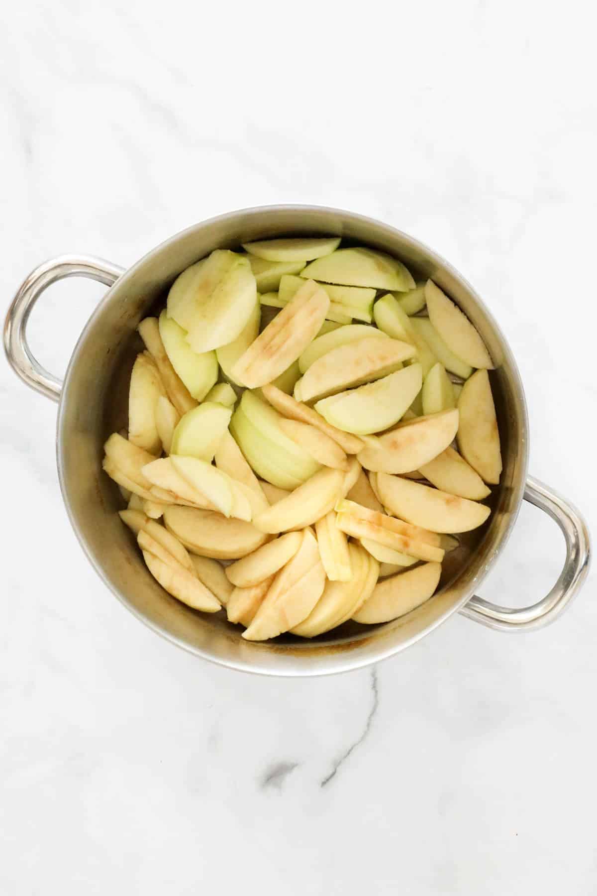 Sliced peeled apples in a large pan.