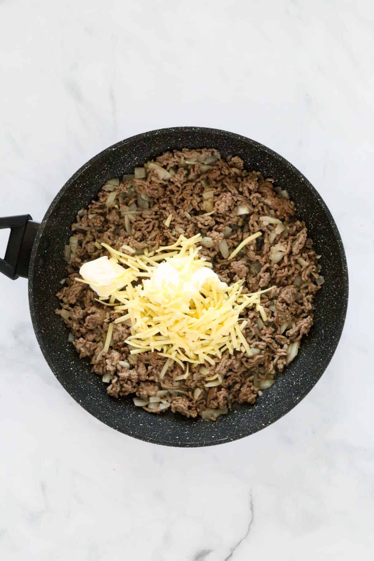 Cream cheese and grated cheese on top of beef mince in a pan.