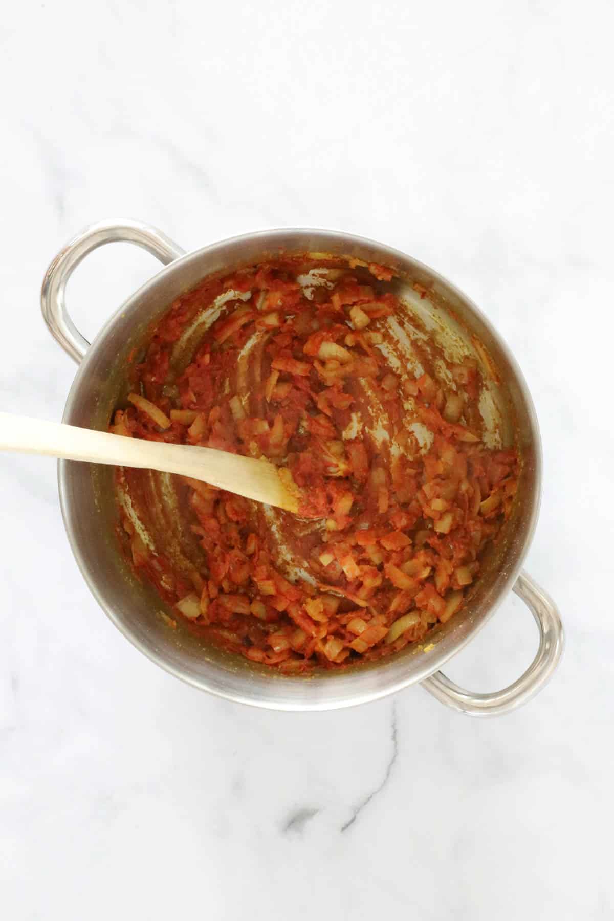 Tomato paste added to sauteed onion in a pot.