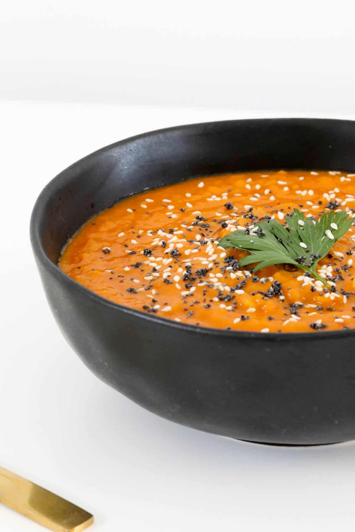 A bowl of carrot soup with herbs and seeds on top.