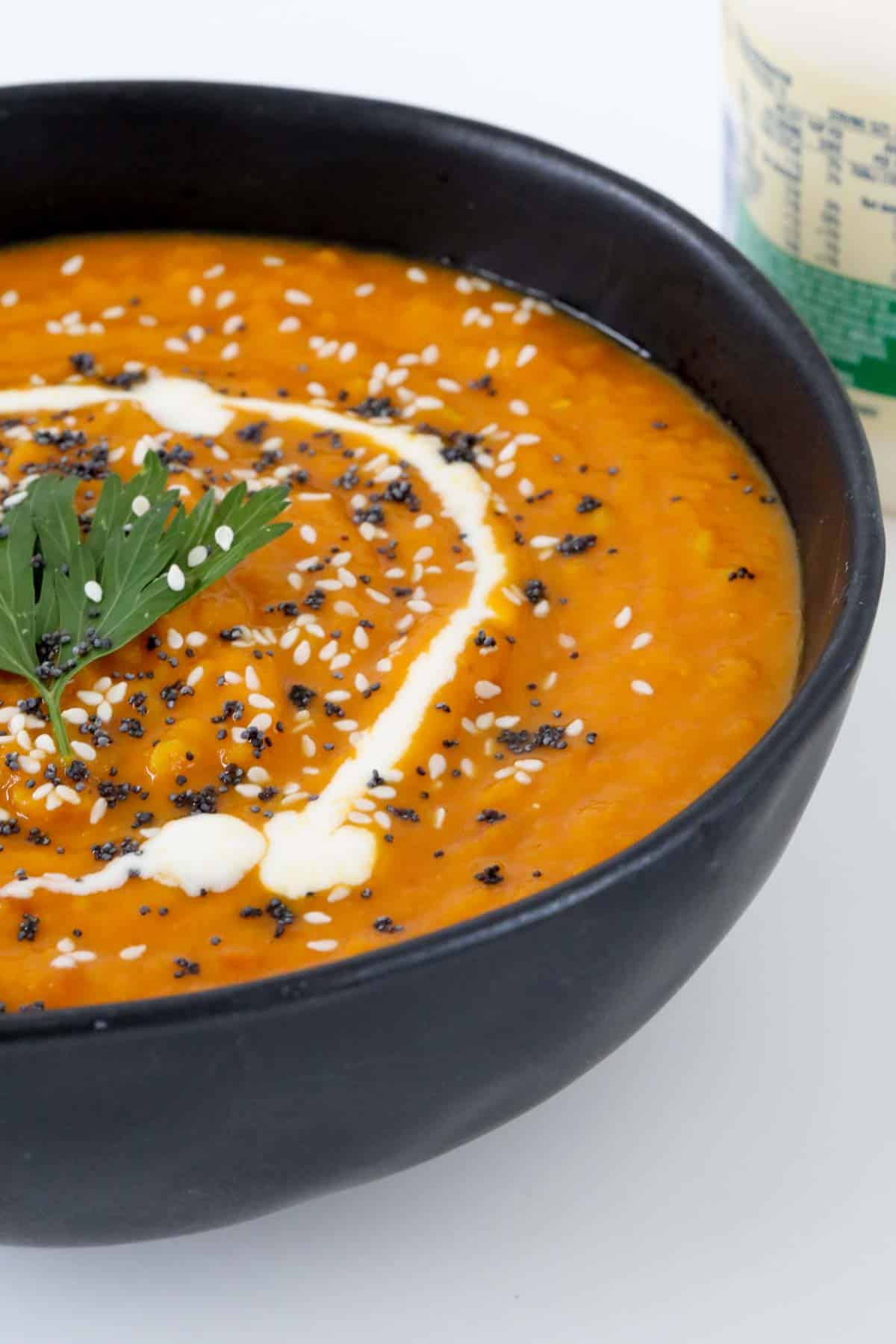 A dollop of cream, sesame seeds and coriander on top of a thick orange soup.