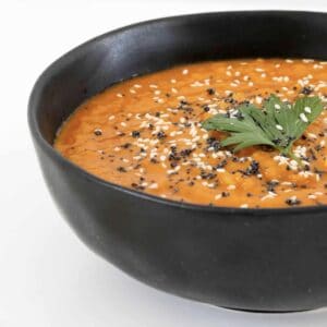 A bowl of carrot soup with herbs and seeds on top.