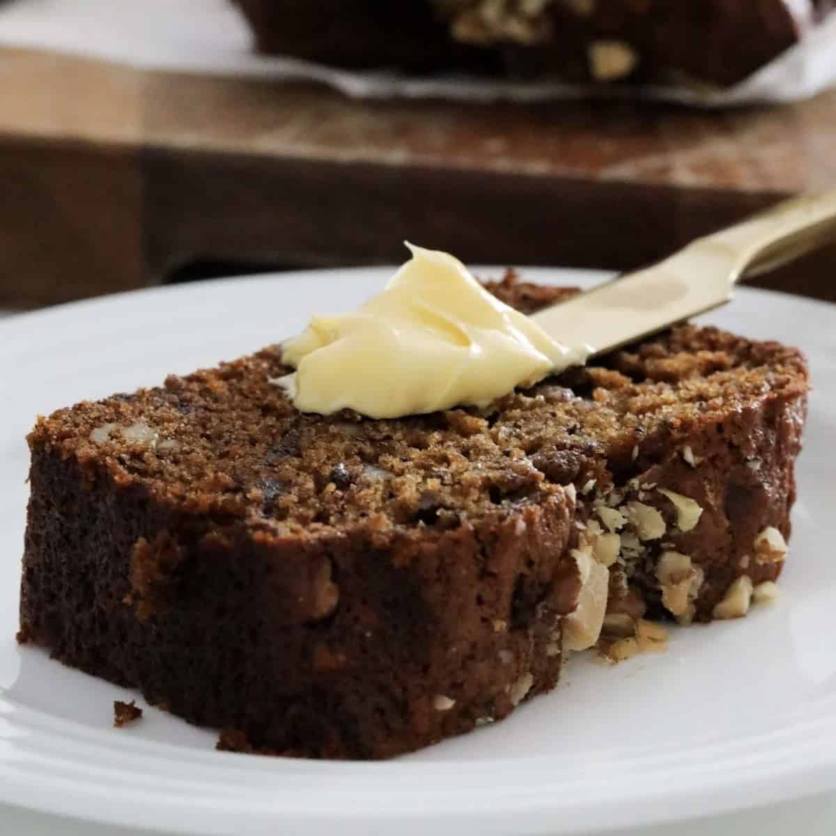 A piece of date walnut loaf being slathered with butter.