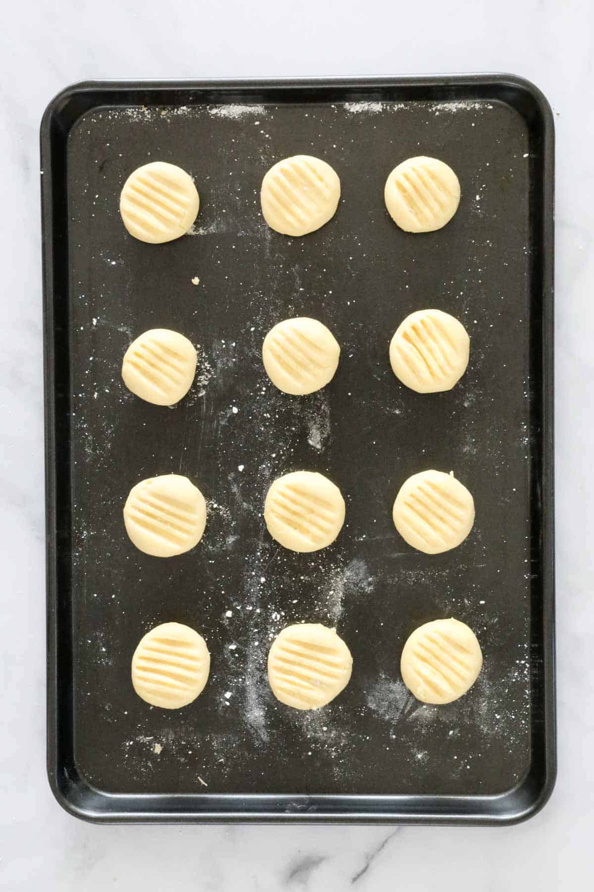 Small biscuits on a baking tray, slightly flattened with a fork.