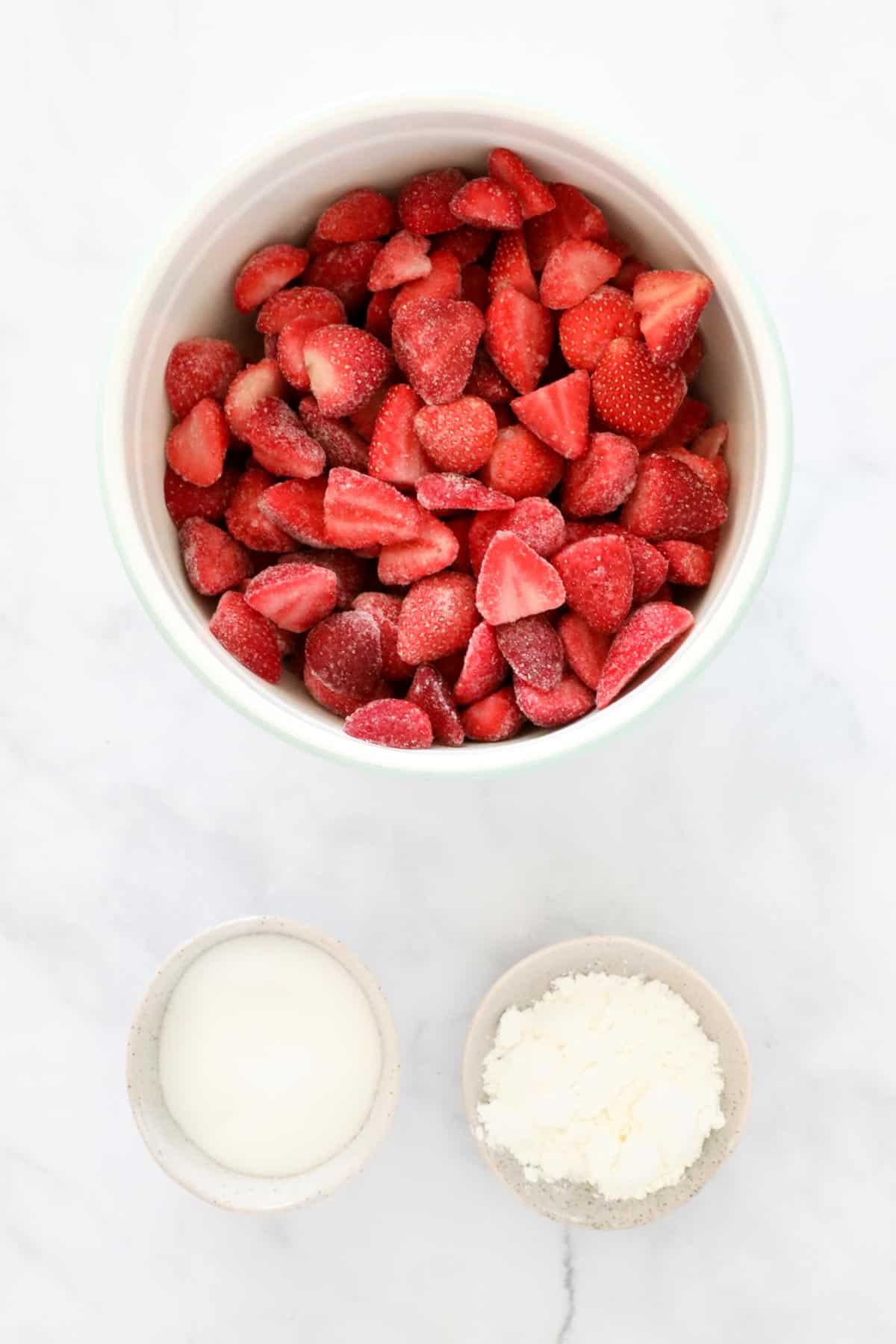 Frozen and halved strawberries, cornflour and sugar in individual bowls.