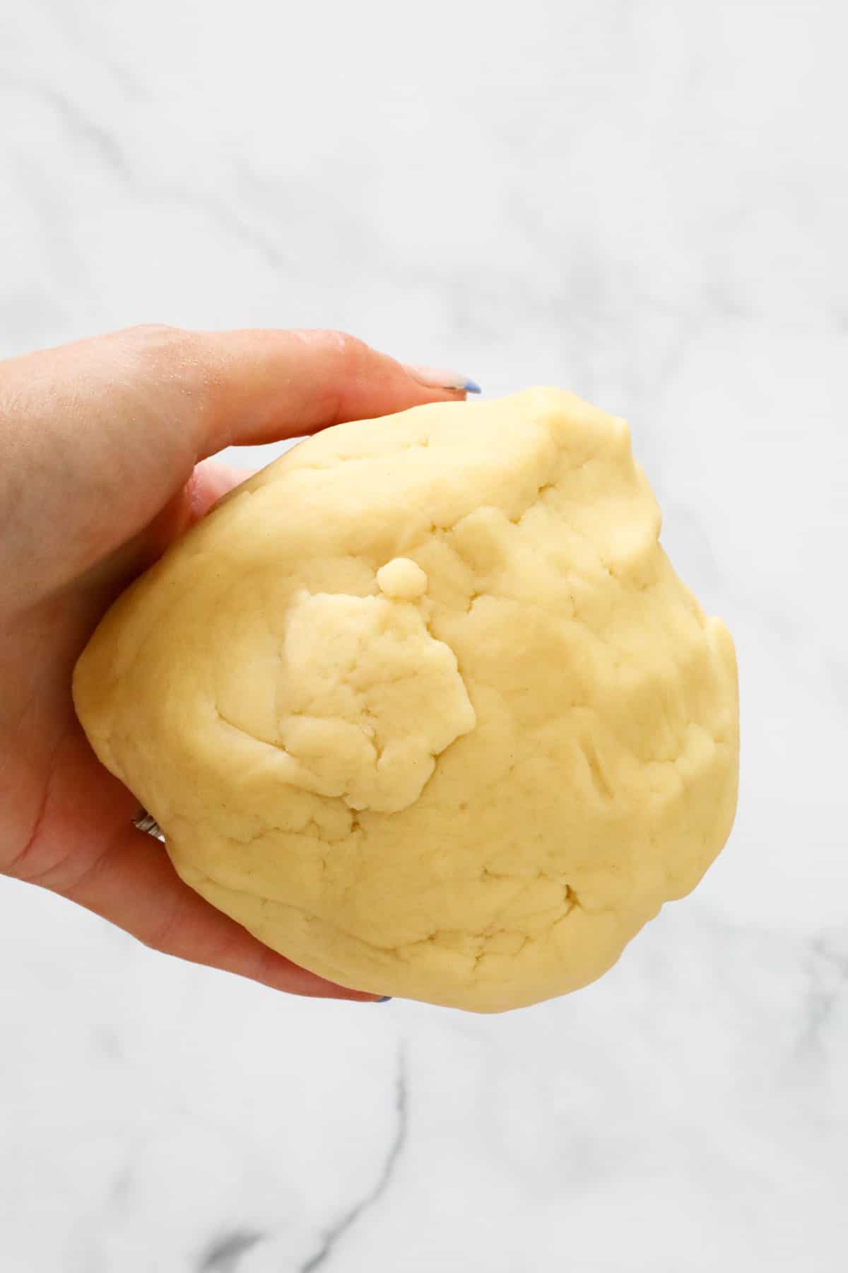 A hand holding a ball of pastry dough.