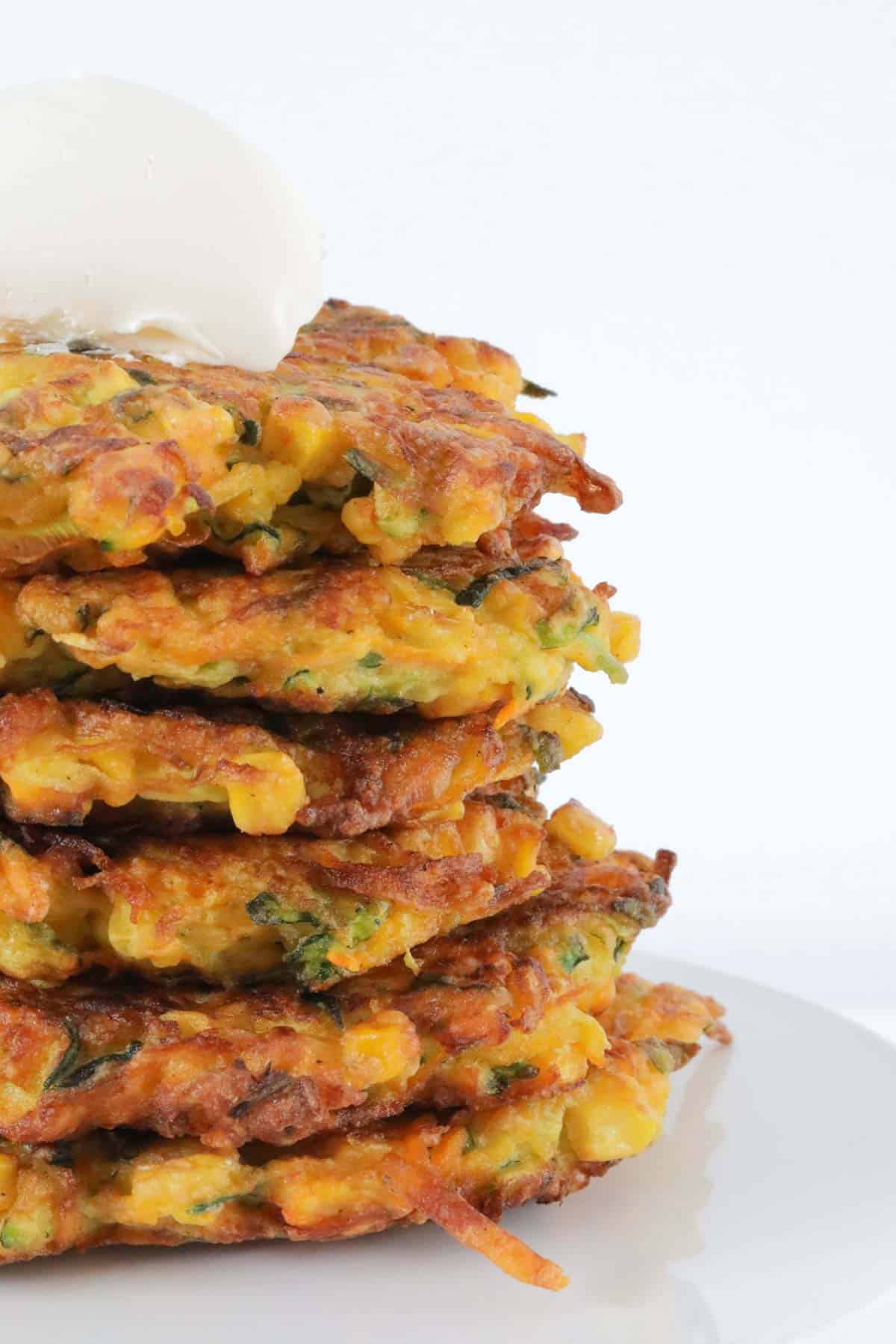 A stack of golden veggie fritters with a dollop of sour cream on top.