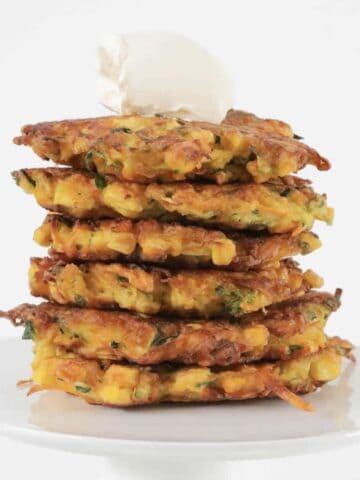 A stack of golden vegetable fritters with sour cream on top.