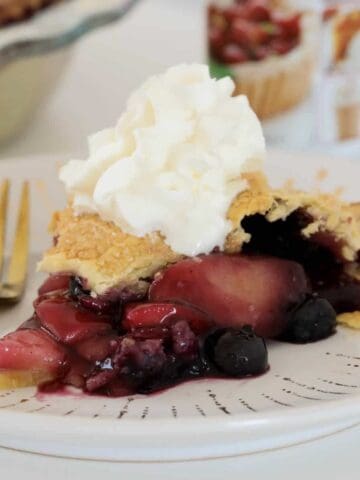 A slice of crispy baked apple blueberry pie with whipped cream on top.