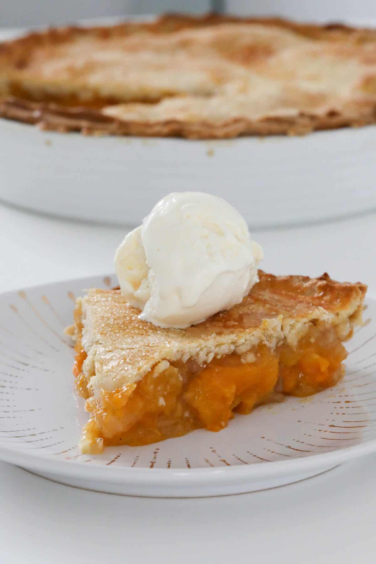 A slice of apricot pie on a plate with a scoop of ice cream on top.