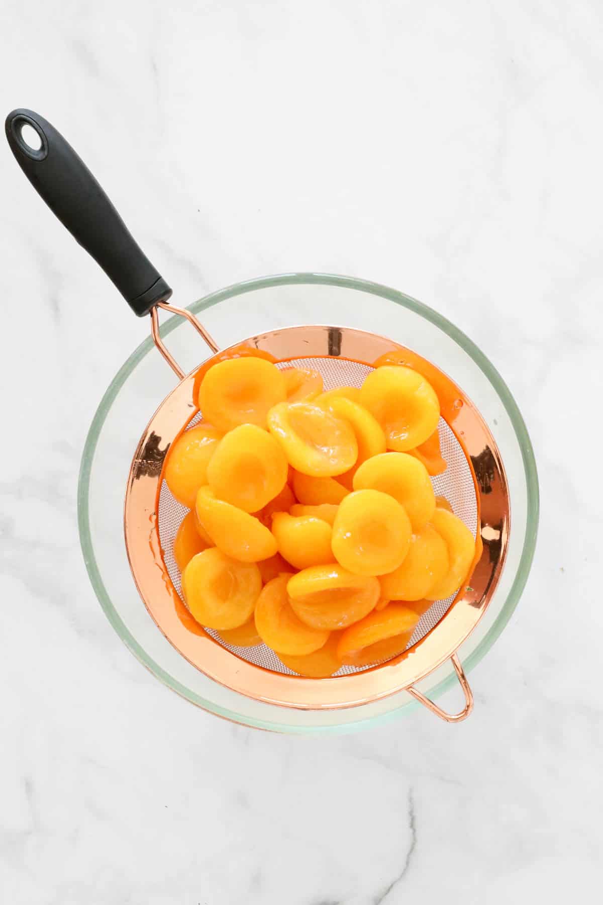 Tinned apricots in a sieve over a bowl.