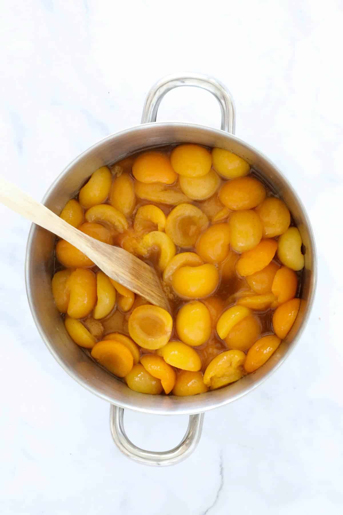 Tinned apricot halves added to the sugar syrup in a saucepan.