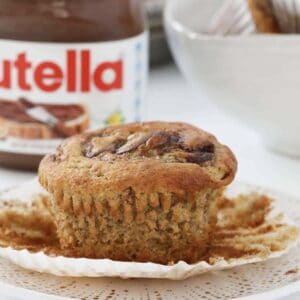 A banana muffin swirled with Nutella in front of a jar of chocolate hazelnut spread.