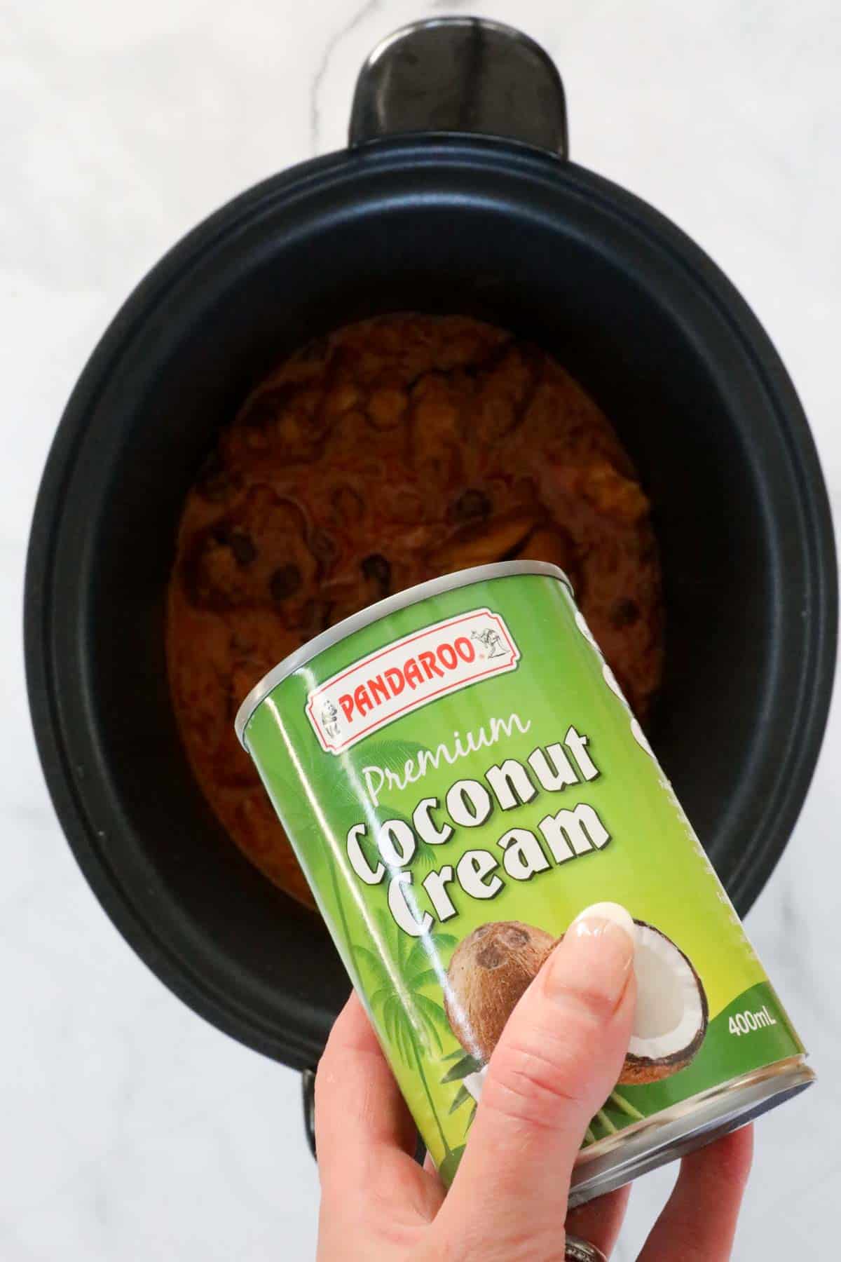 A can of coconut cream being poured into the slow cooker.