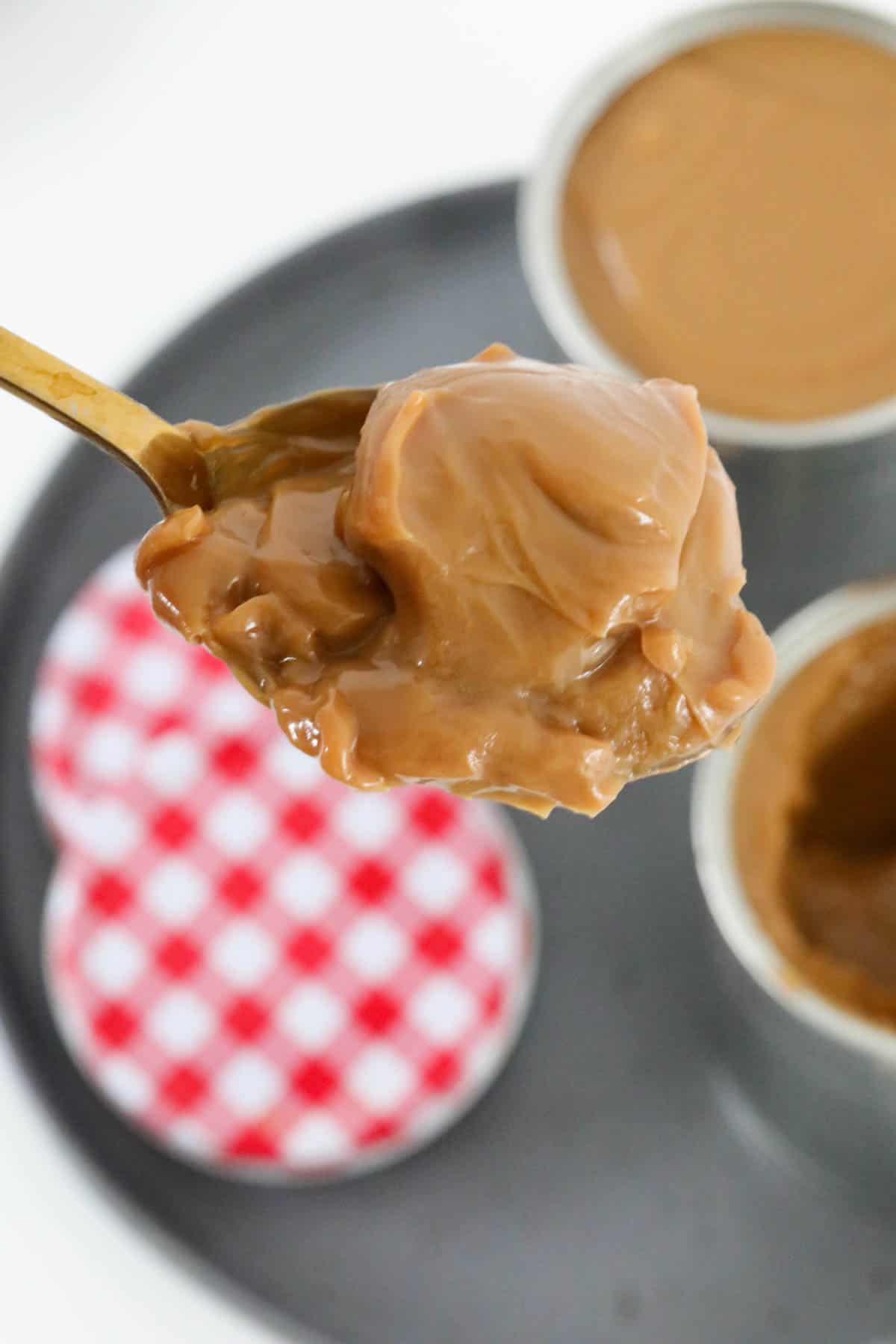 A close up of a spoon holding thickened condensed milk turned a caramel colour.