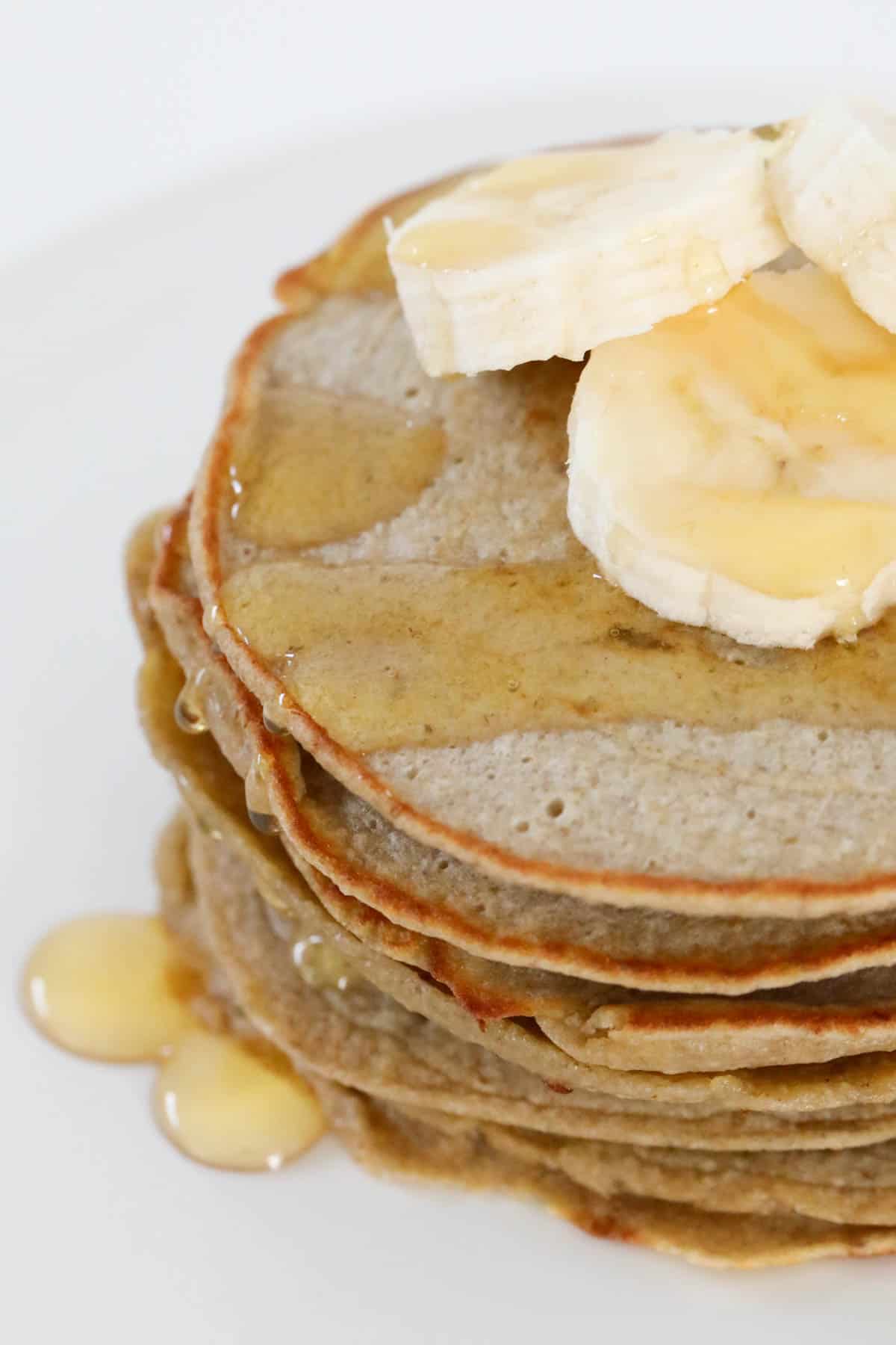 A stack of banana oat pancakes topped with sliced bananas and drizzled with maple syrup.