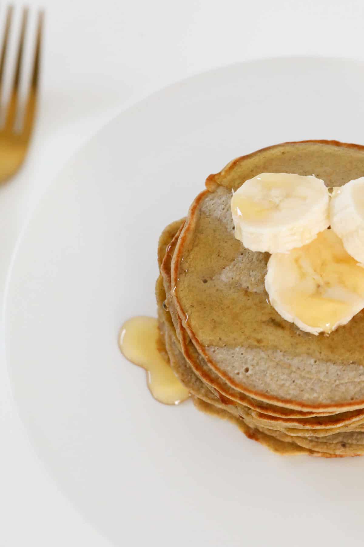 A stack of pancakes with syrup and sliced banana on a plate with a fork ready to eat.