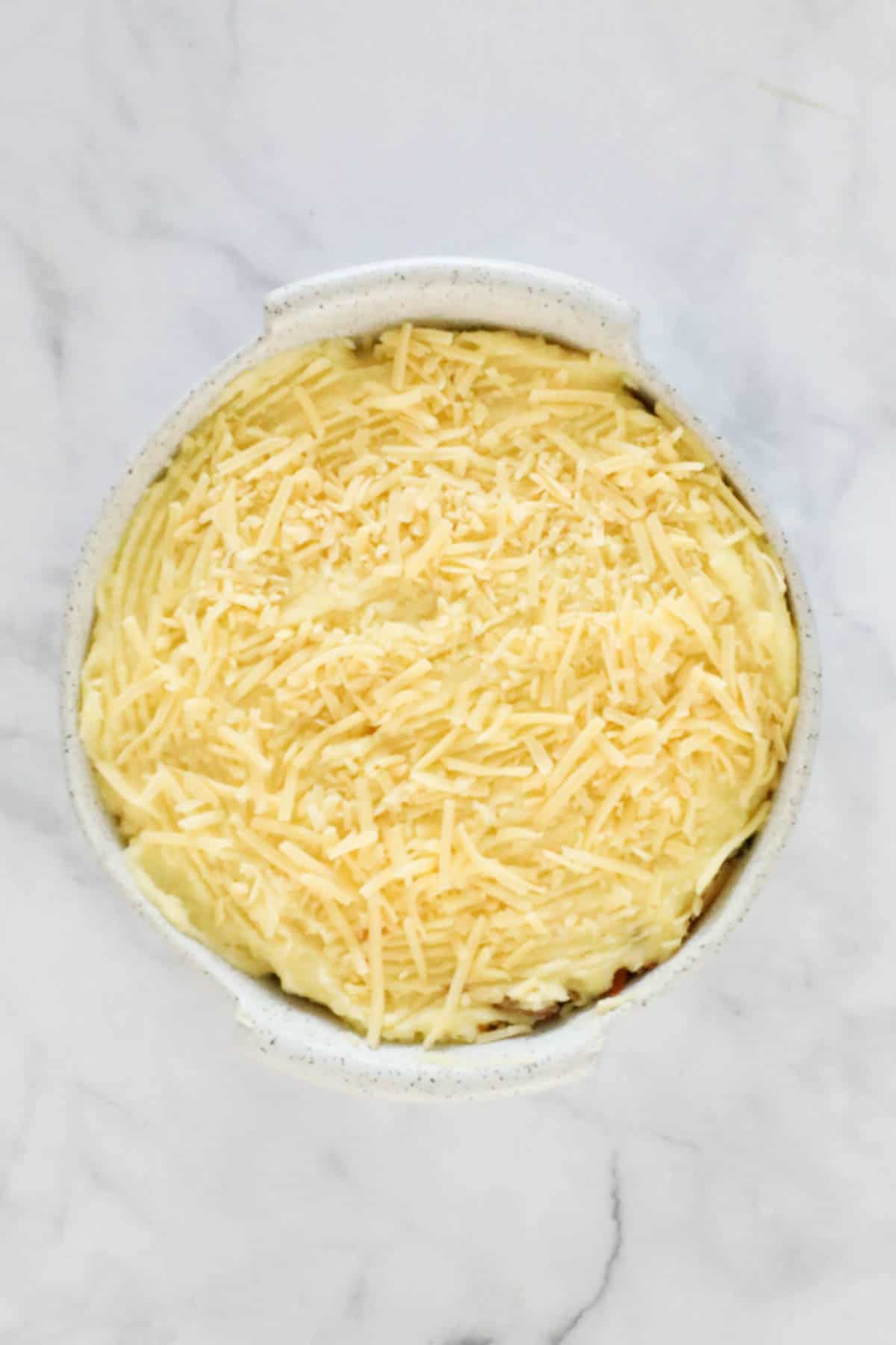 Mashed potato and grated cheese in a round baking dish.