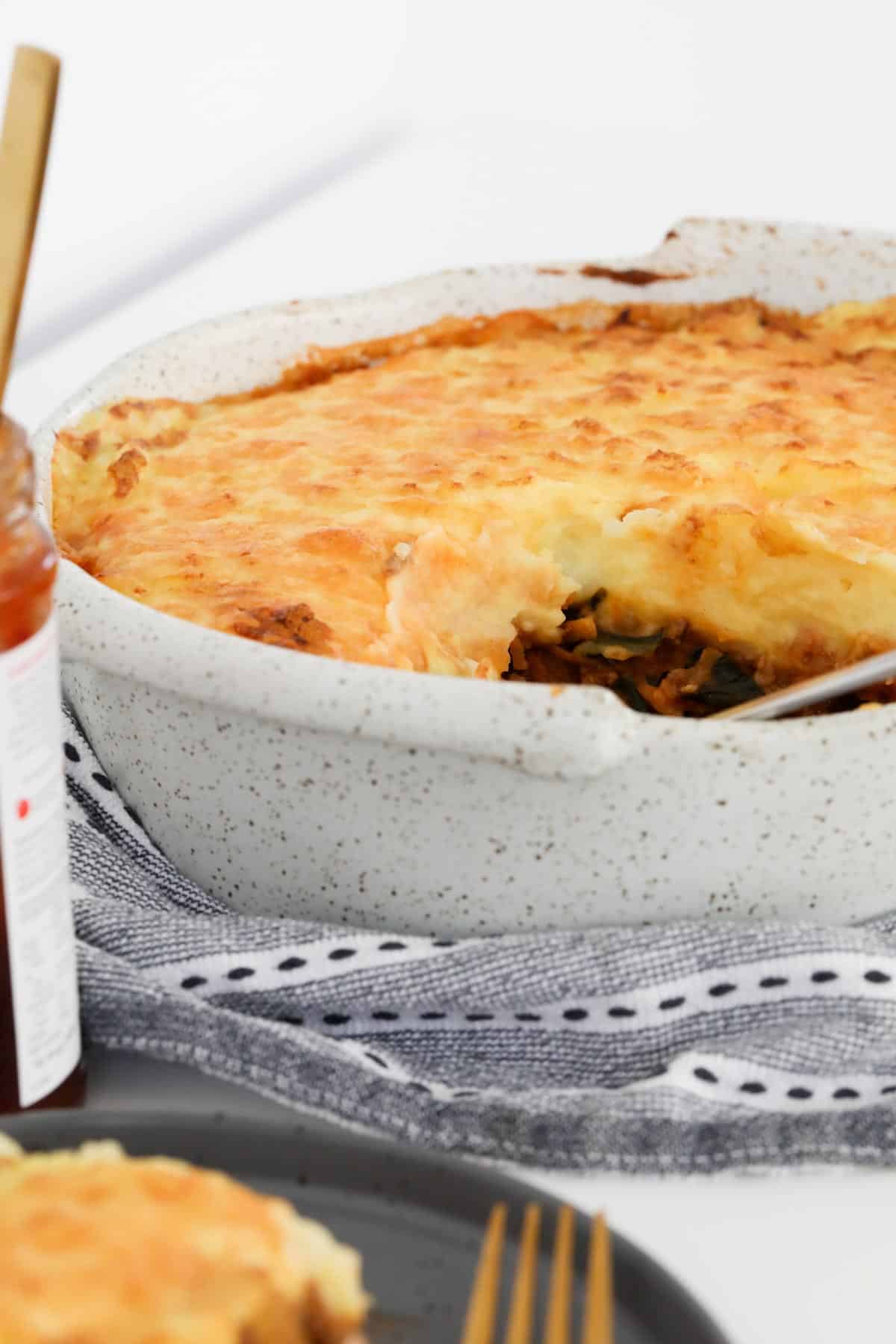 A spoon in a baking dish filled with beef and potato pie.